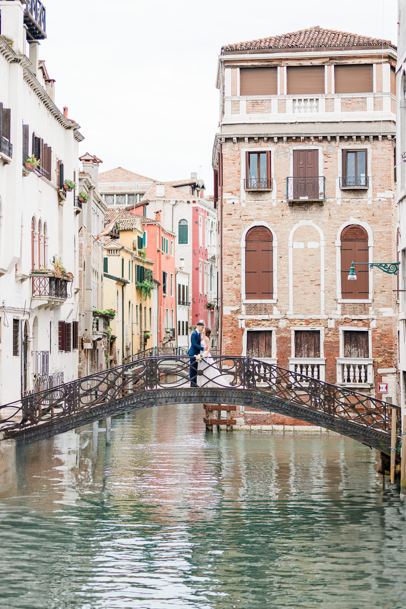 A couple sharing an intimate moment on a small bridge over a Venetian canal, surrounded by historic buildings.