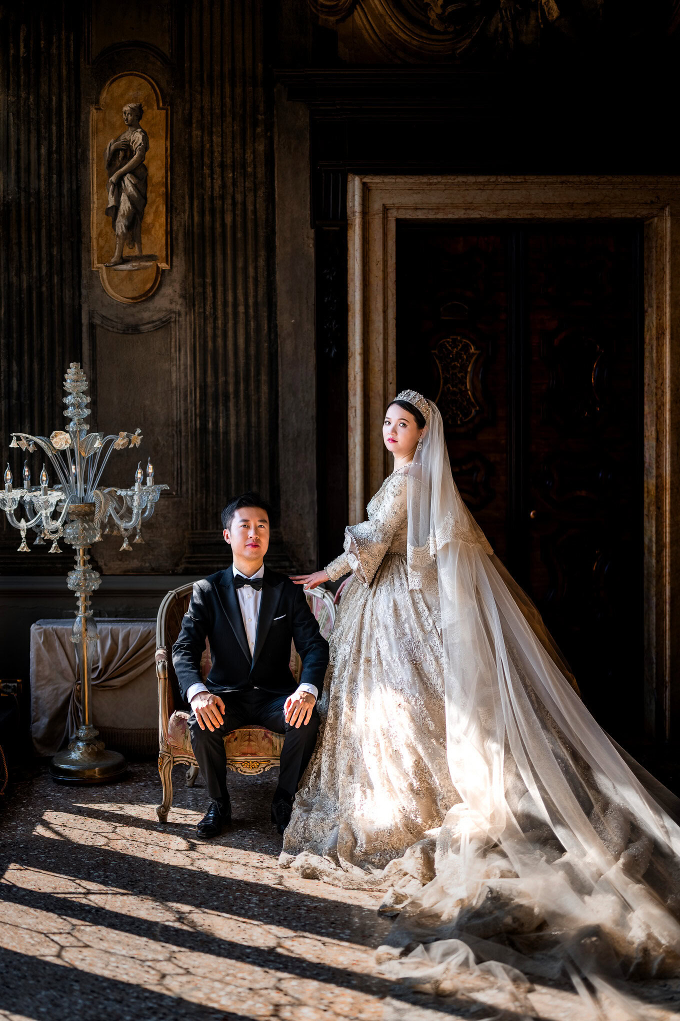 A couple in elegant attire sharing an intimate moment inside a richly decorated Venetian interior.