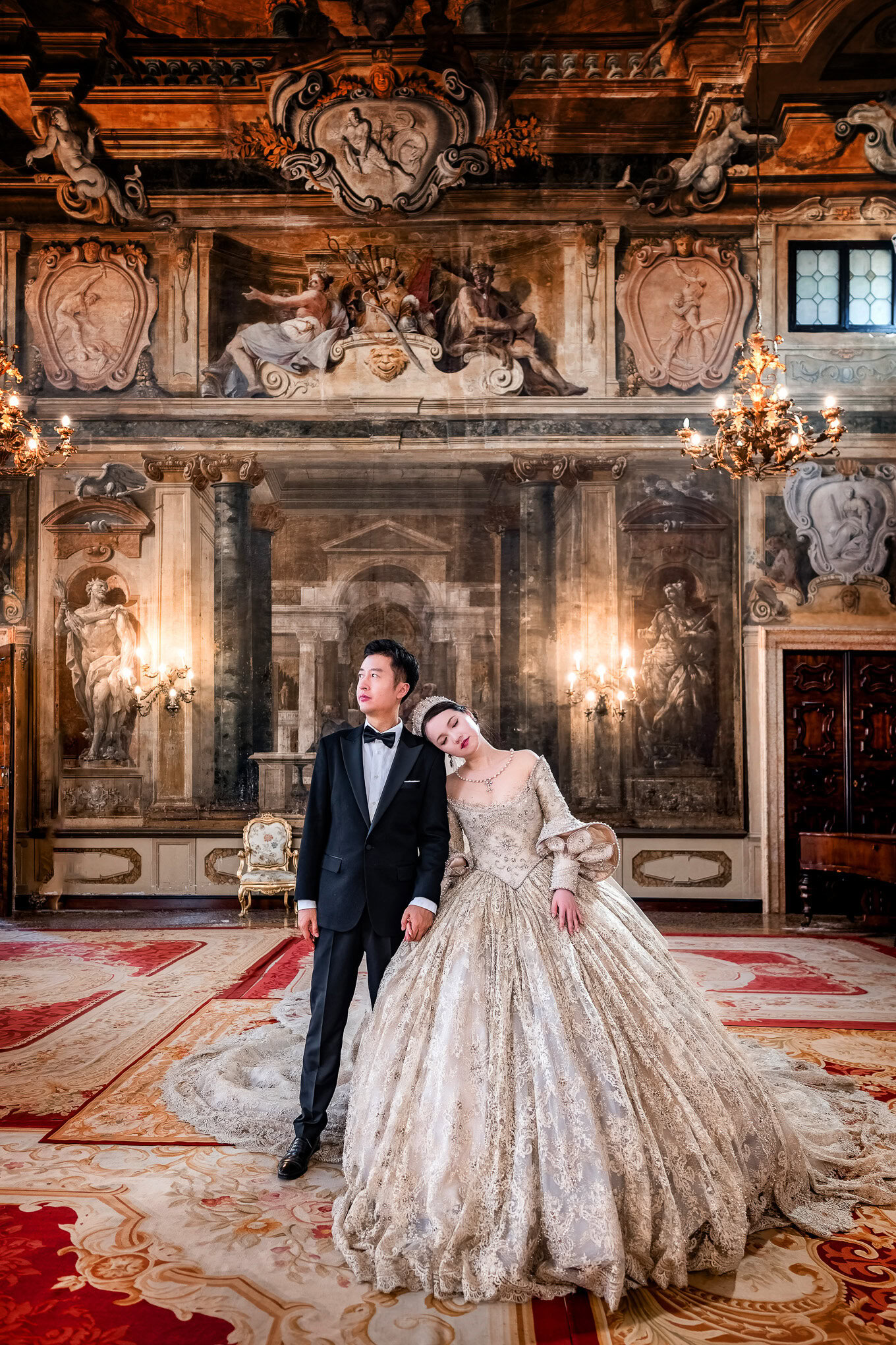 A detailed, intimate couple in elegant wedding attire standing in a richly decorated Venetian palace interior.