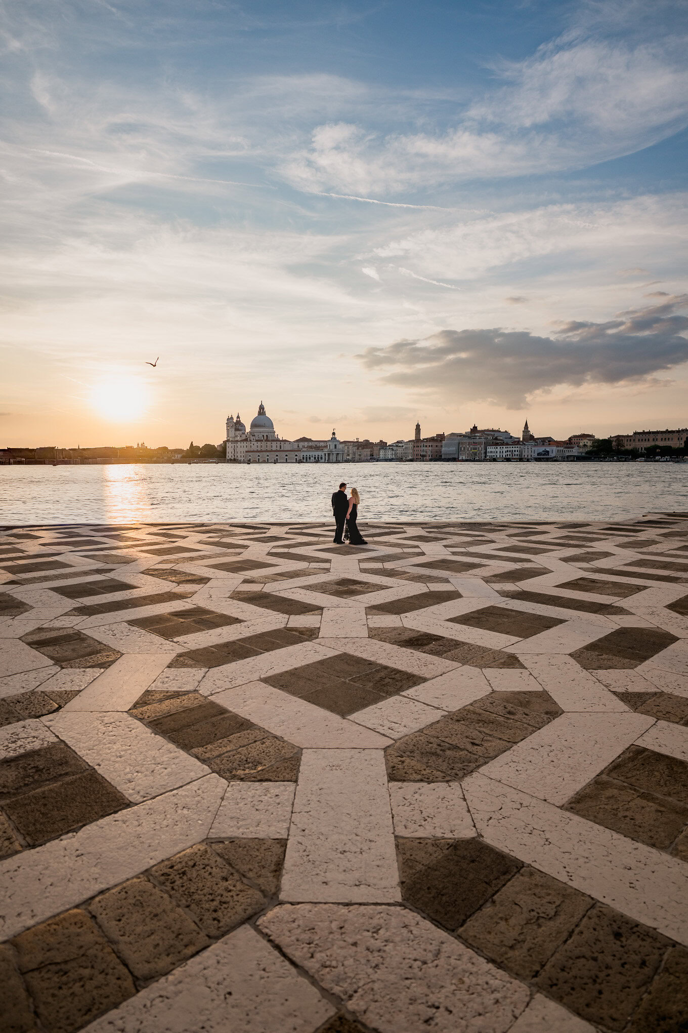A couple sharing an intimate moment on a Venetian waterfront at sunset, with soft light illuminating.