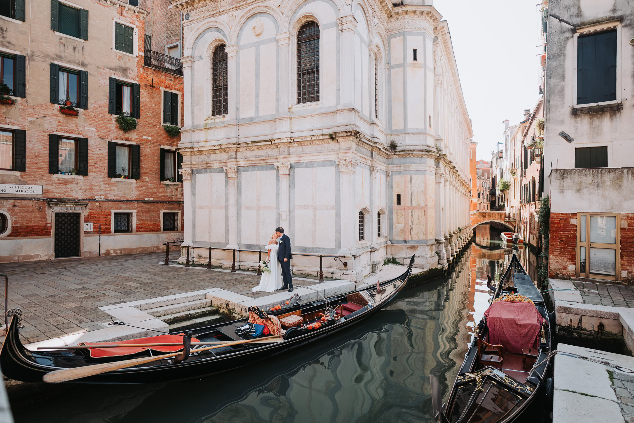 Intimate couple sharing a quiet moment beside a canal in Venice, bathed in soft natural light and surrounded by historic.