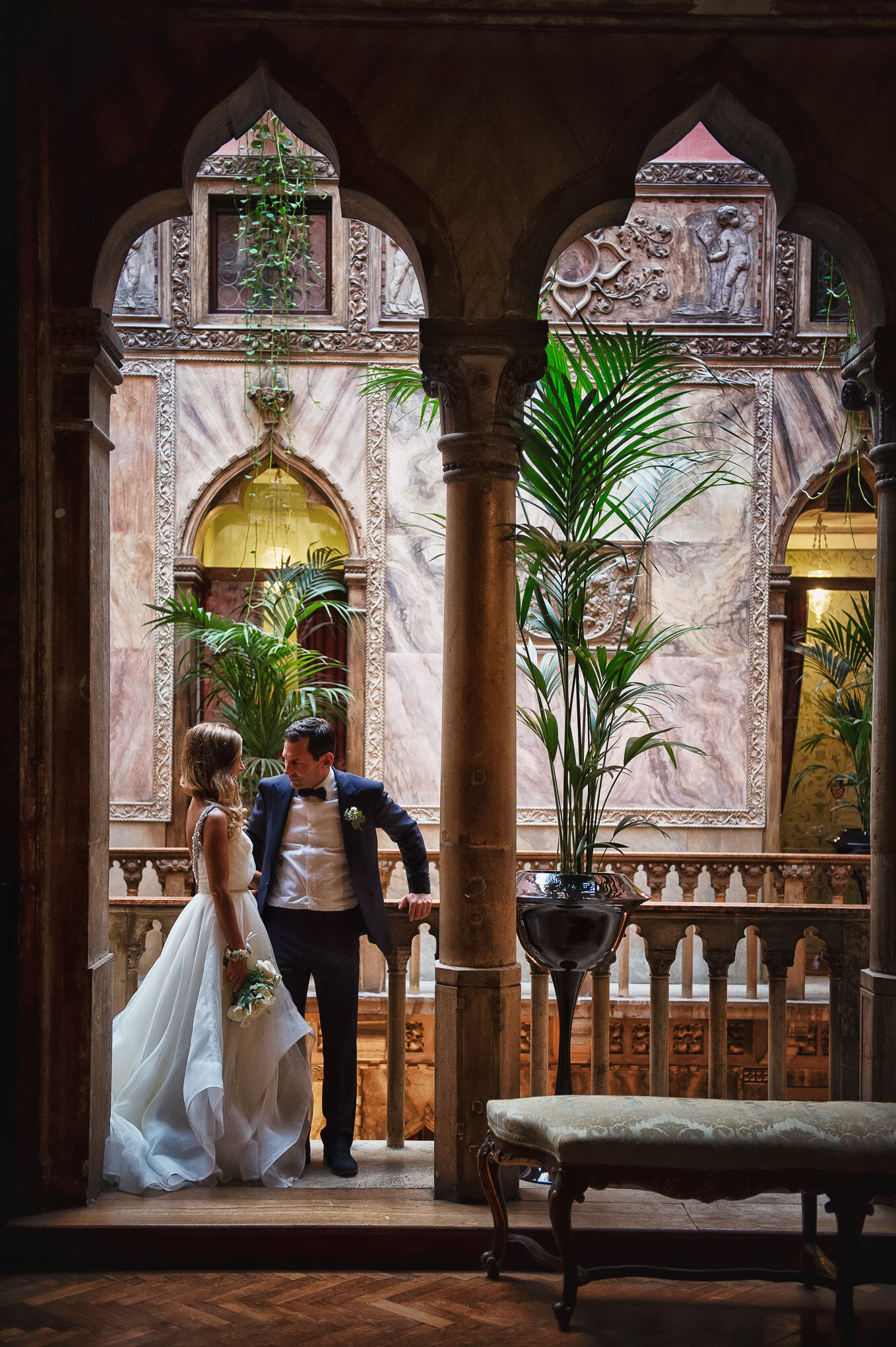 Intimate couple sharing a tender moment on a Venetian balcony surrounded by lush greenery and ornate architecture.