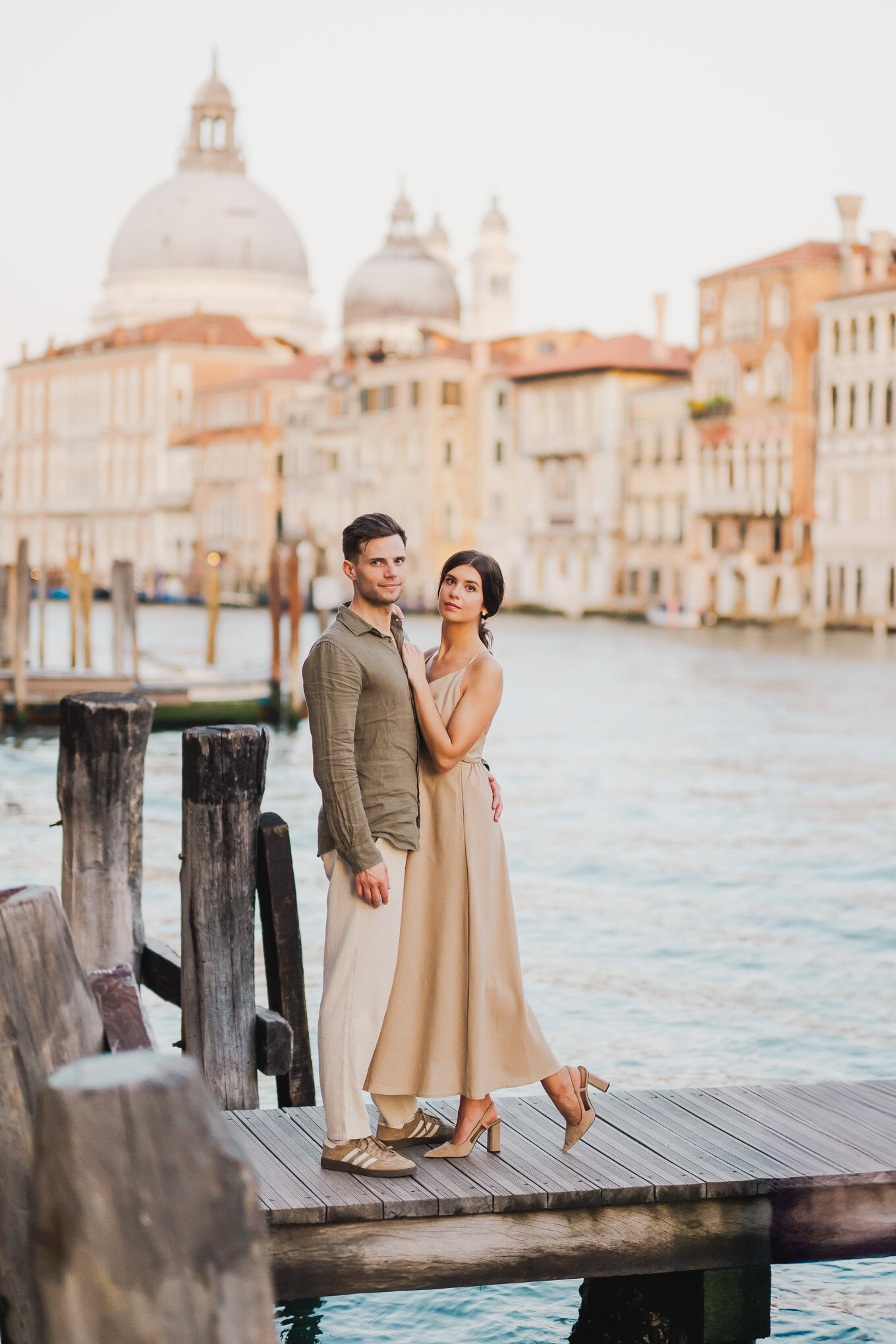 A couple standing on a wooden dock by the water with Venice's historic skyline and domed churches in.