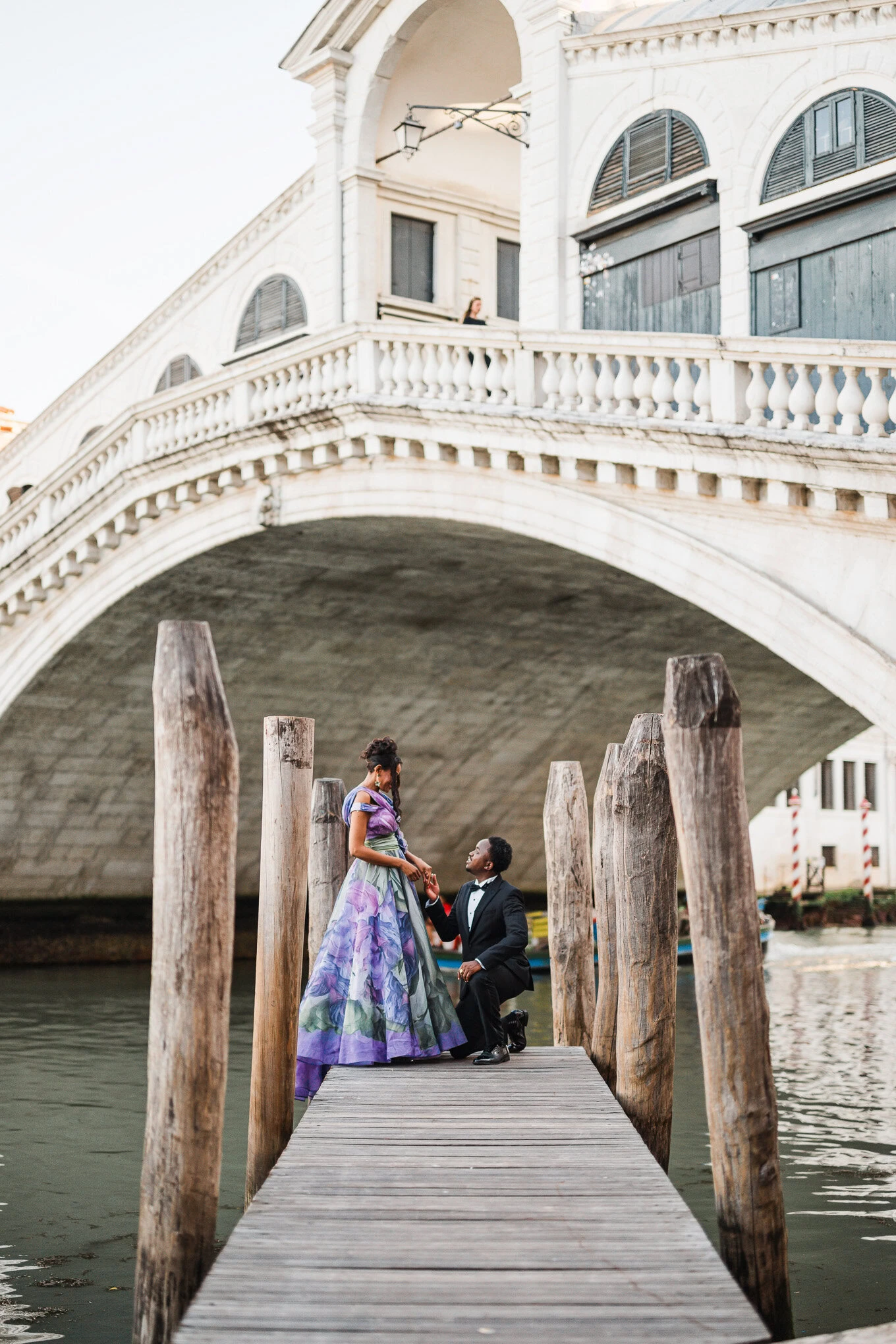 A couple sharing a romantic moment on a wooden dock beneath a historic bridge in Venice, bathed in s.