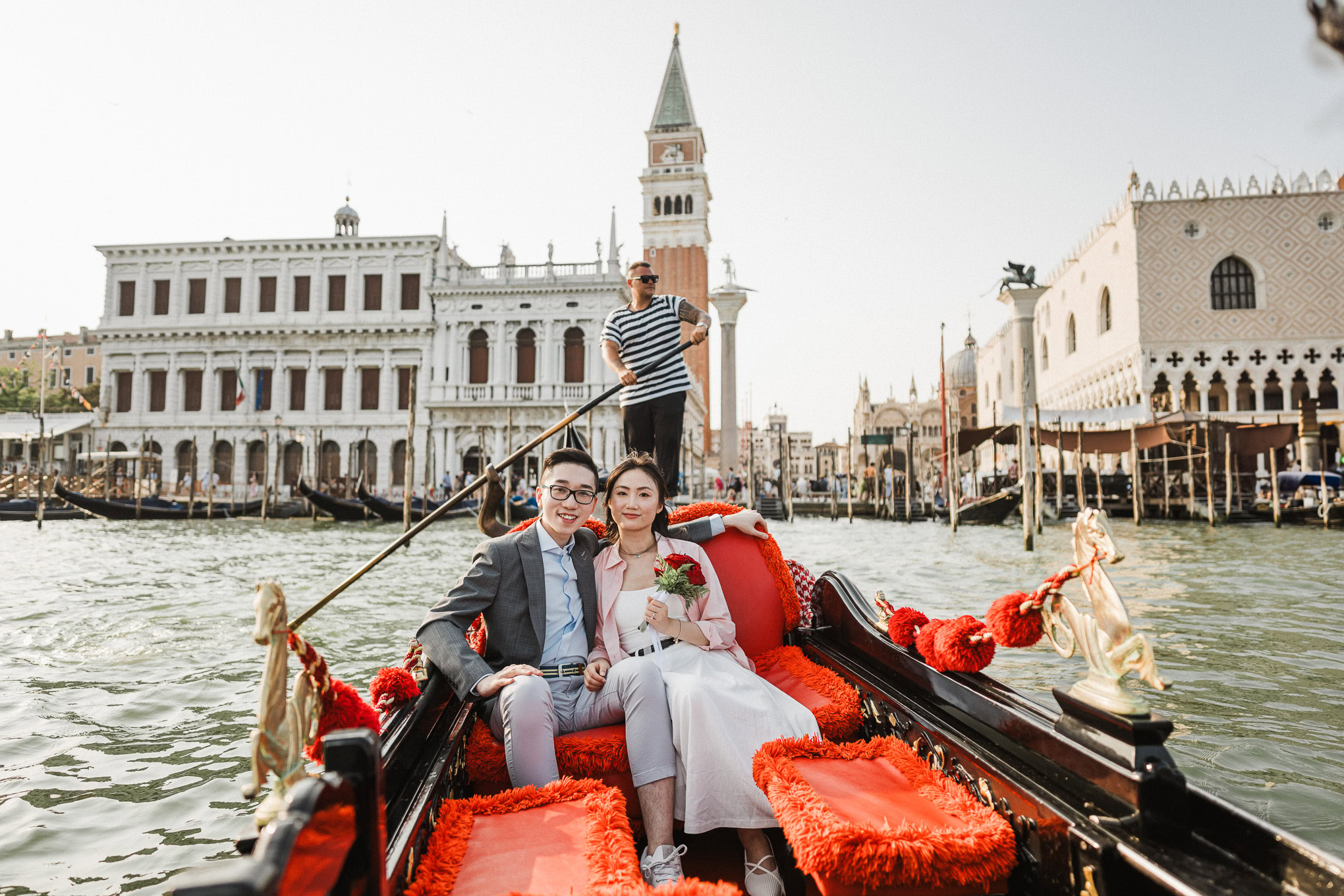 Romantic couple enjoying a gondola ride through Venice's historic canals on a sunny day.