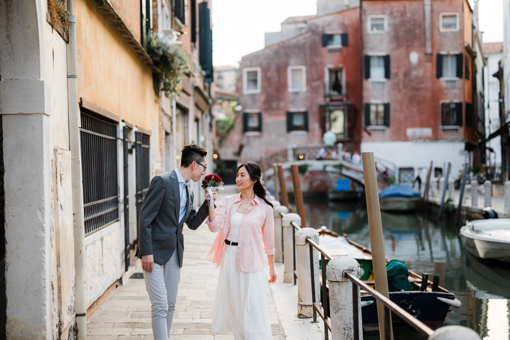 A couple sharing a tender moment along a canal in Venice, bathed in soft natural light, evoking roma.