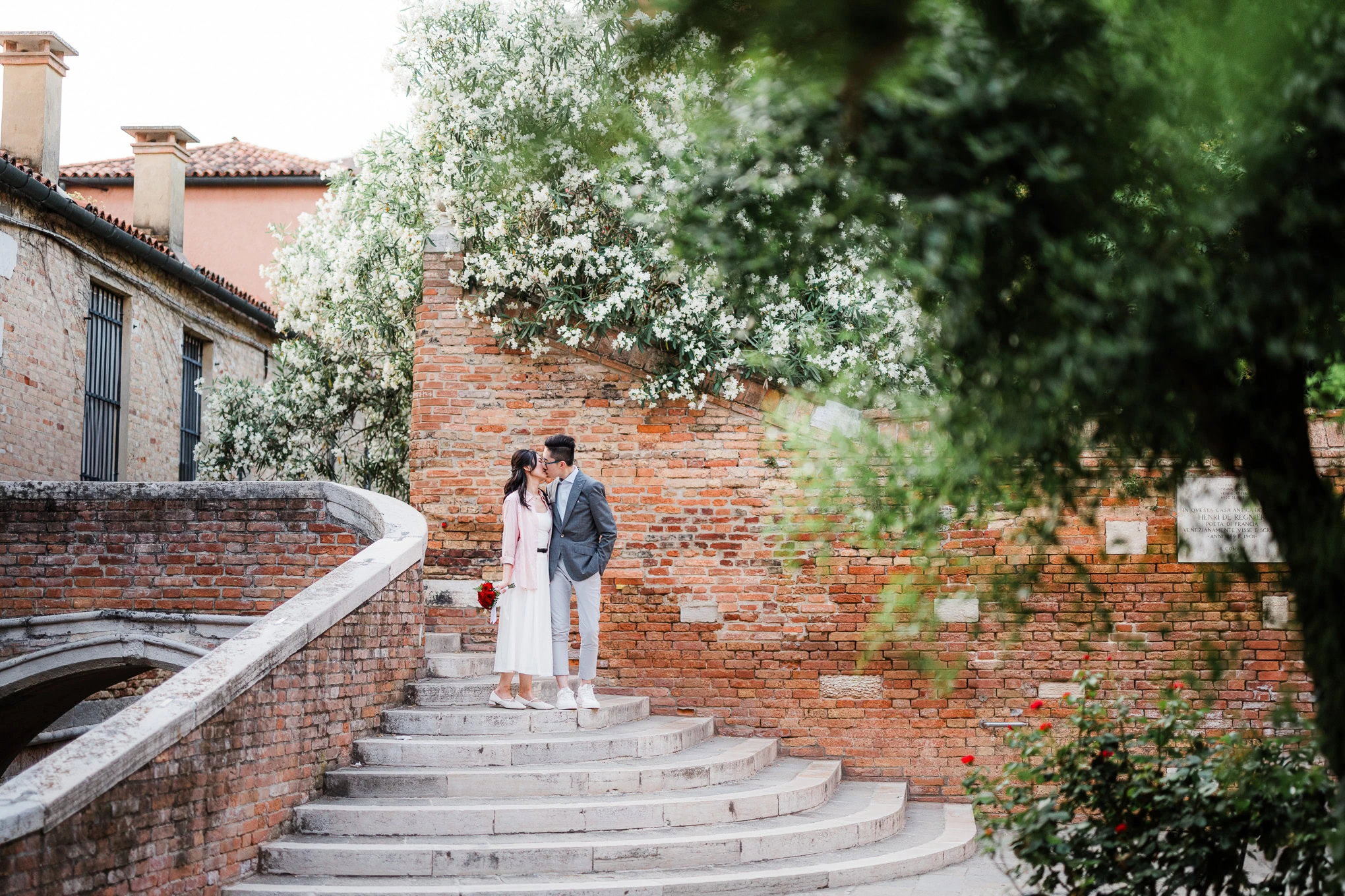 A couple sharing an intimate moment on a stone staircase surrounded by lush greenery and blooming tr.