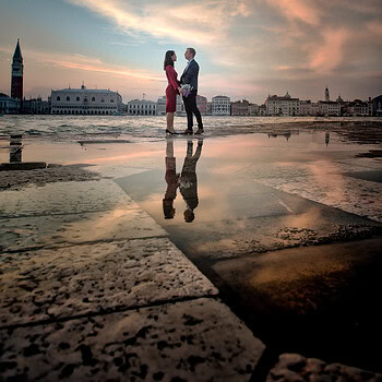 A woman and a man holding hands on a reflective wet surface at sunset, with a city skyline and drama.