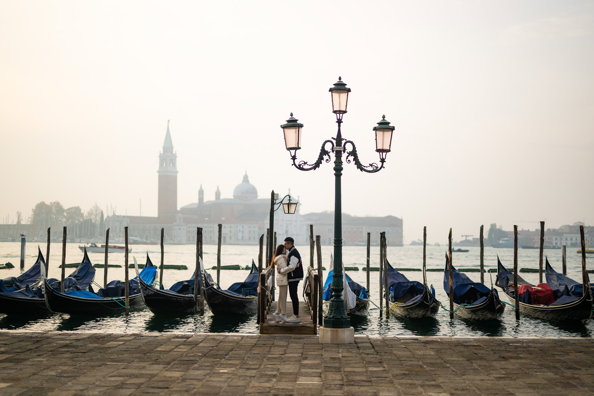 A serene scene of a couple embracing by the water in Venice, with gondolas and historic architecture.