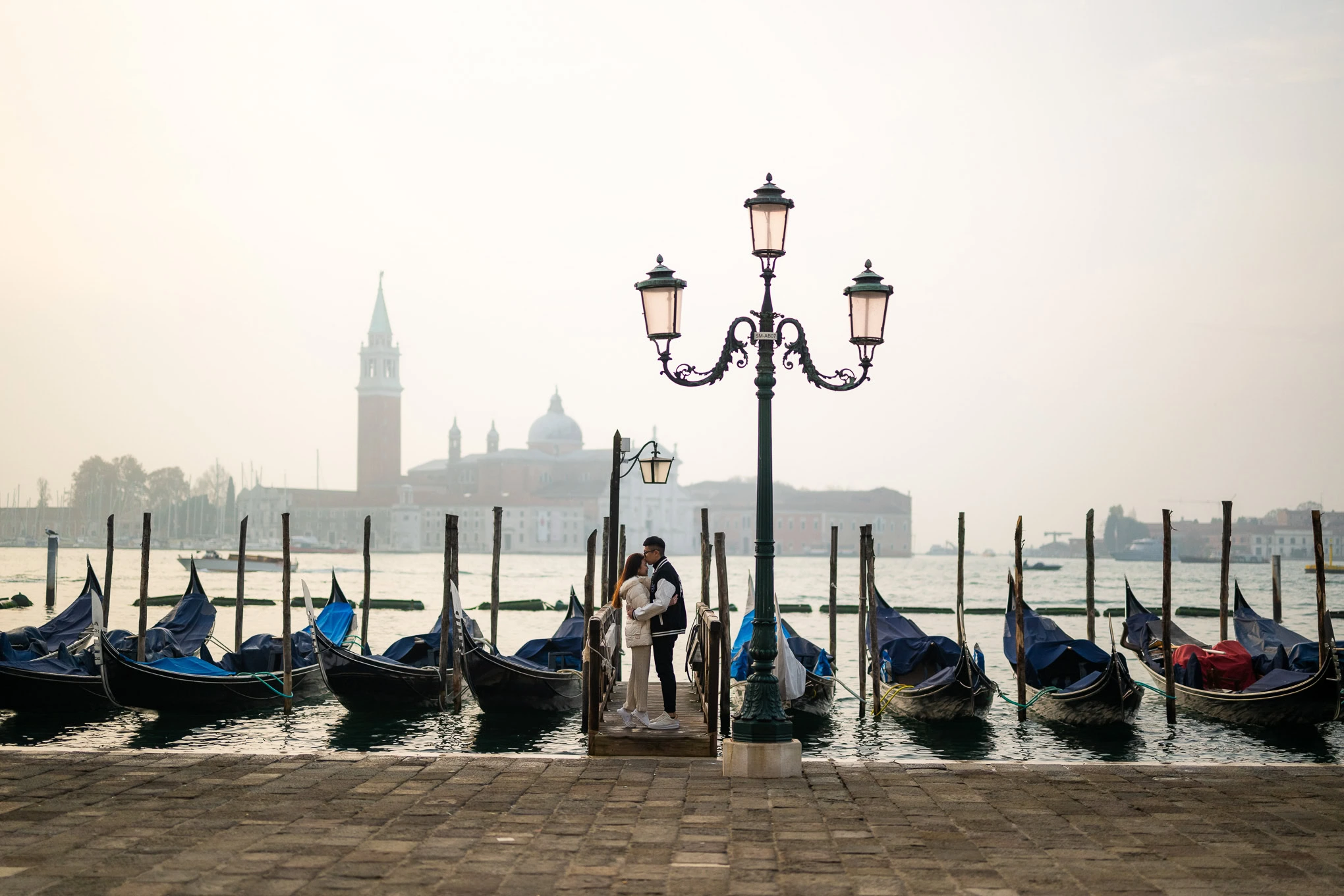 A serene scene of a couple embracing by the water in Venice, with gondolas and historic architecture.