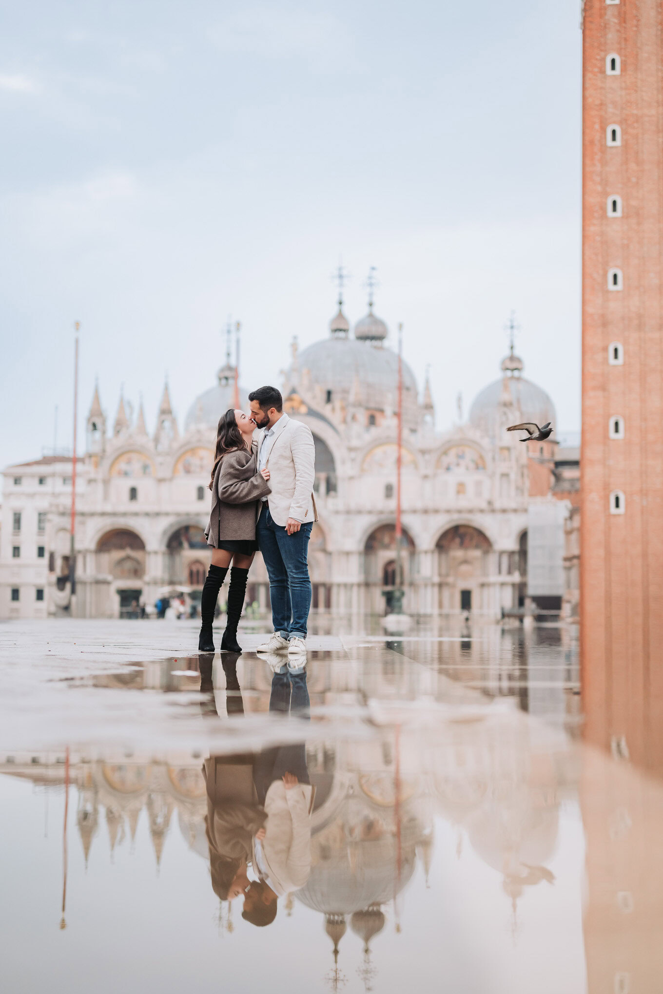 A couple sharing an intimate moment on a rainy day in front of a historic European cathedral, reflec.
