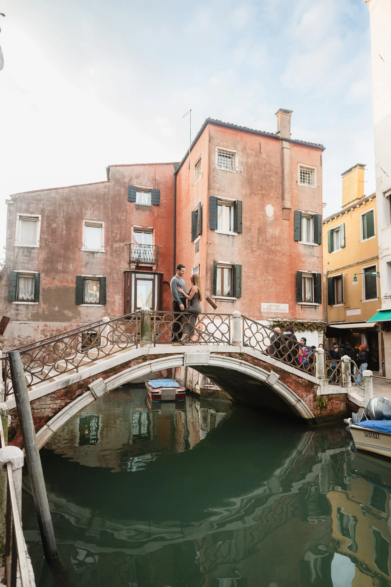 A woman and a child stand on a small bridge over a canal in a colorful, weathered neighborhood under.