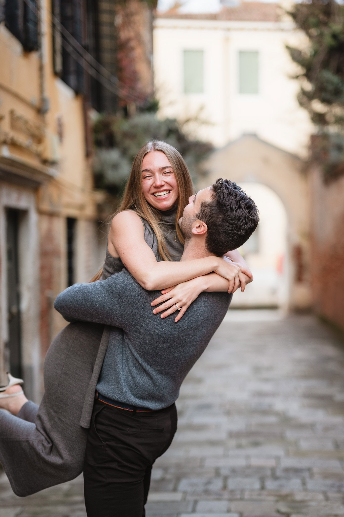A joyful couple sharing a tender moment on a charming cobblestone street, bathed in soft natural lig.