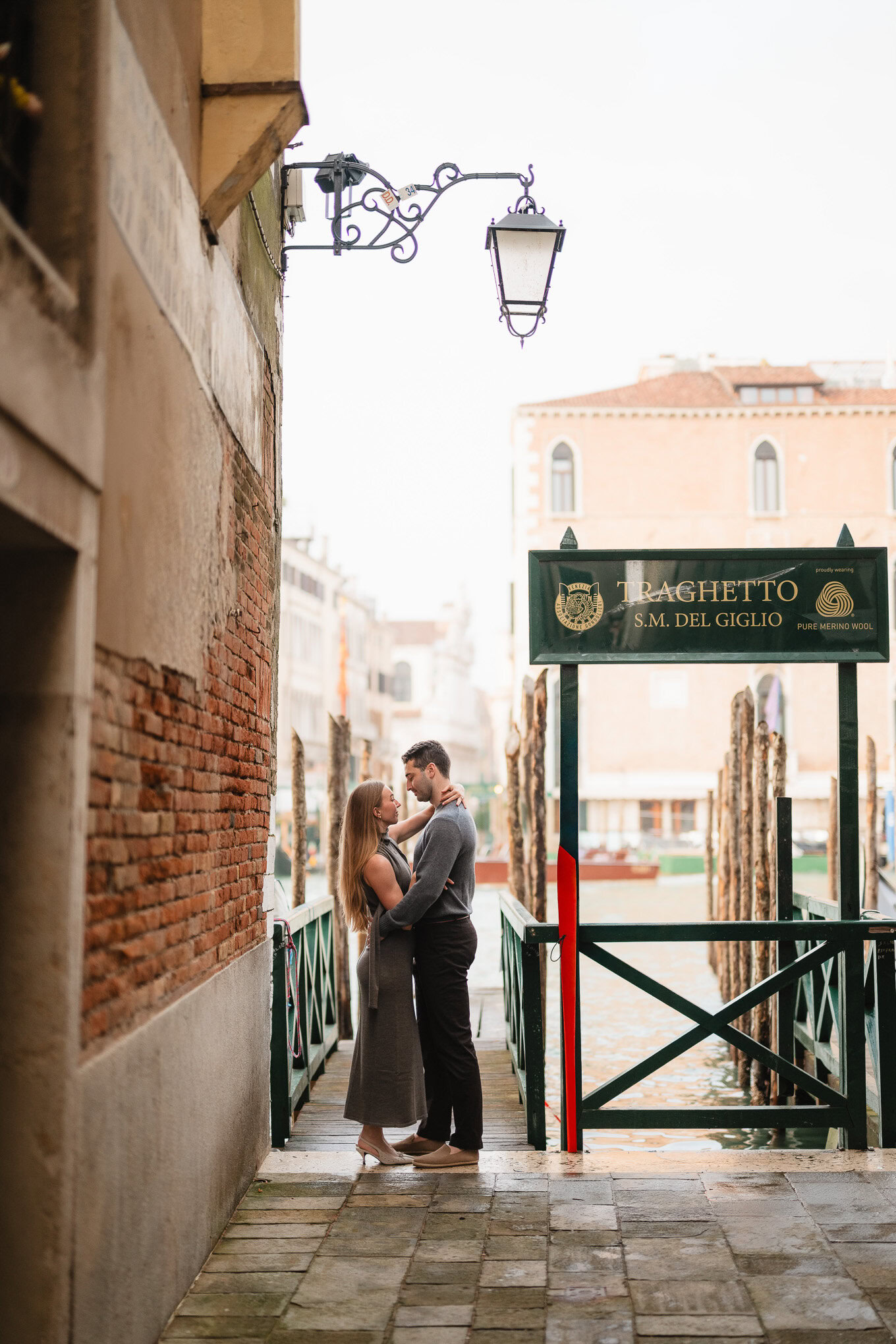 A couple embracing on a narrow Venice canal walkway at dusk, soft light highlighting their tender mo.