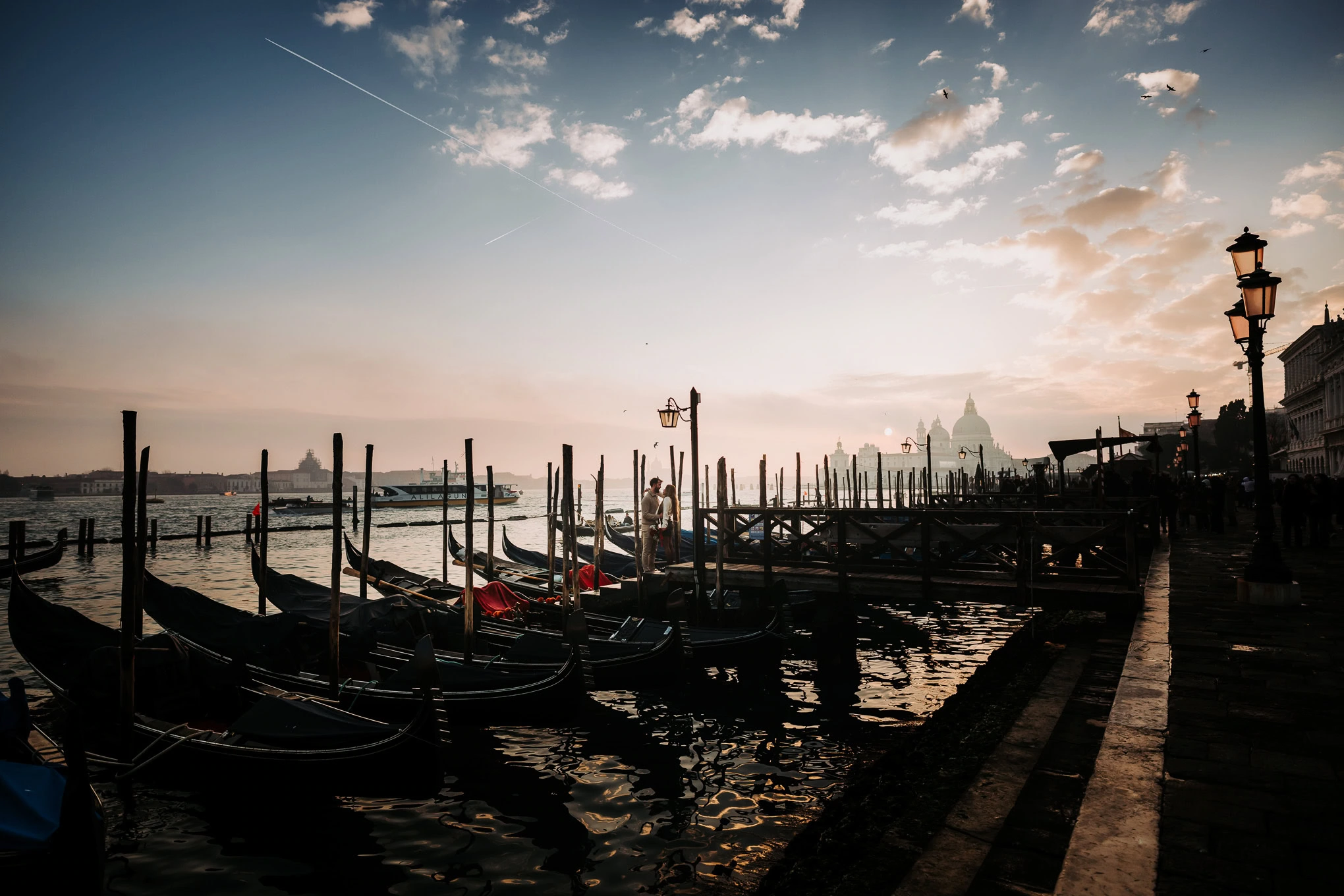A serene scene of gondolas moored along a Venetian canal at sunset, with warm light reflecting on th.