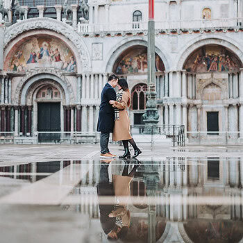 Romantic couple embracing at Piazza San Marco during acqua alta sunrise, reflecting on wet surface.