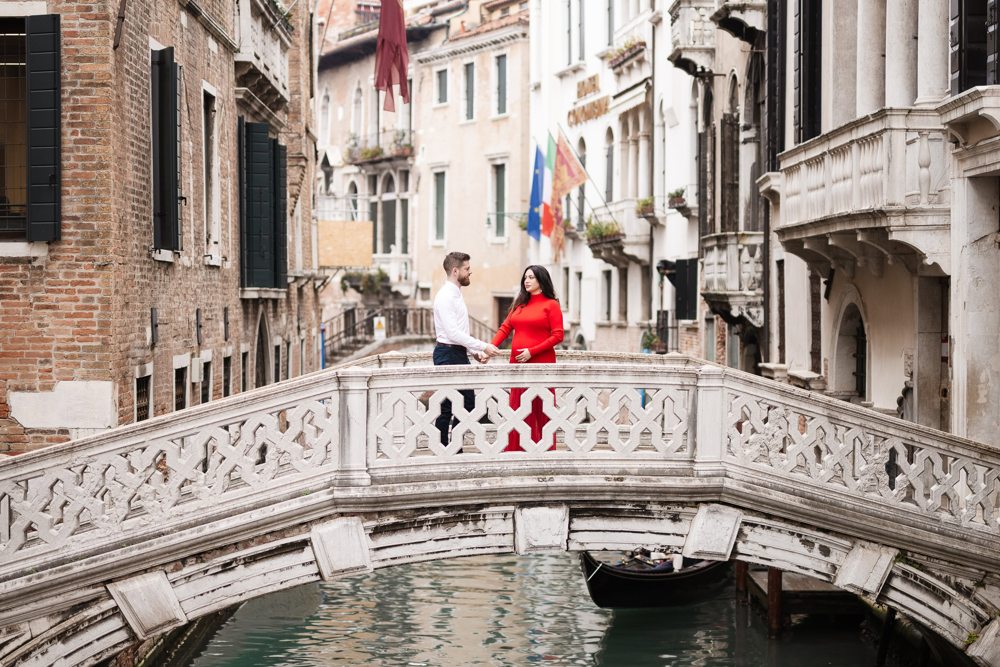 A colorful family interacts on a small bridge over a canal in Venice, surrounded by historic buildings and soft natural.