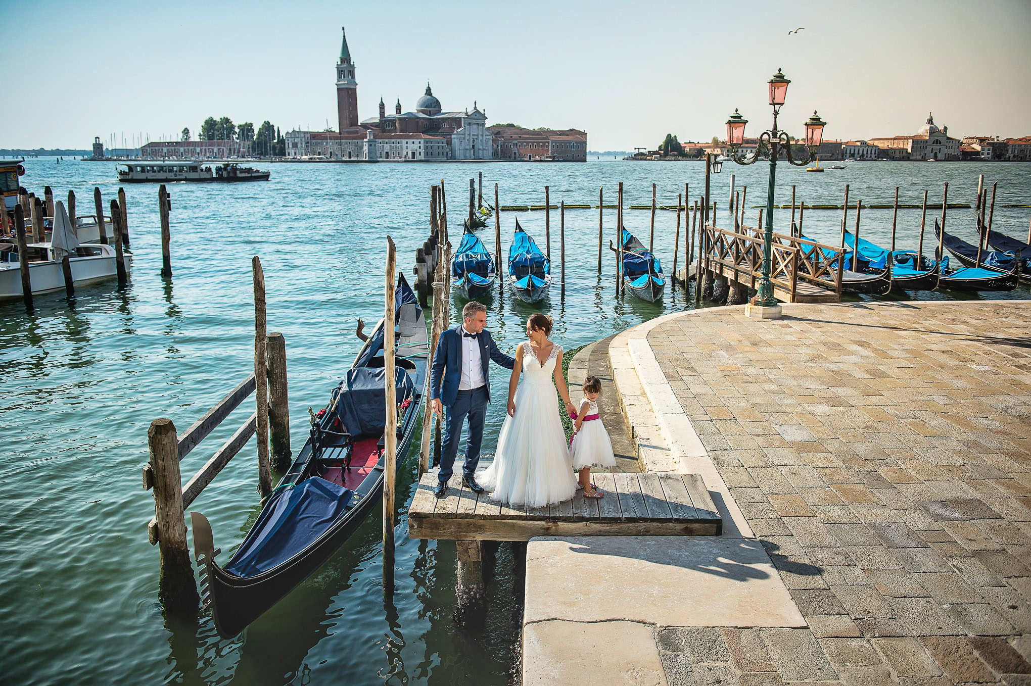Family enjoying a walk and boat ride along Venice's waterfront with historic buildings in the background.