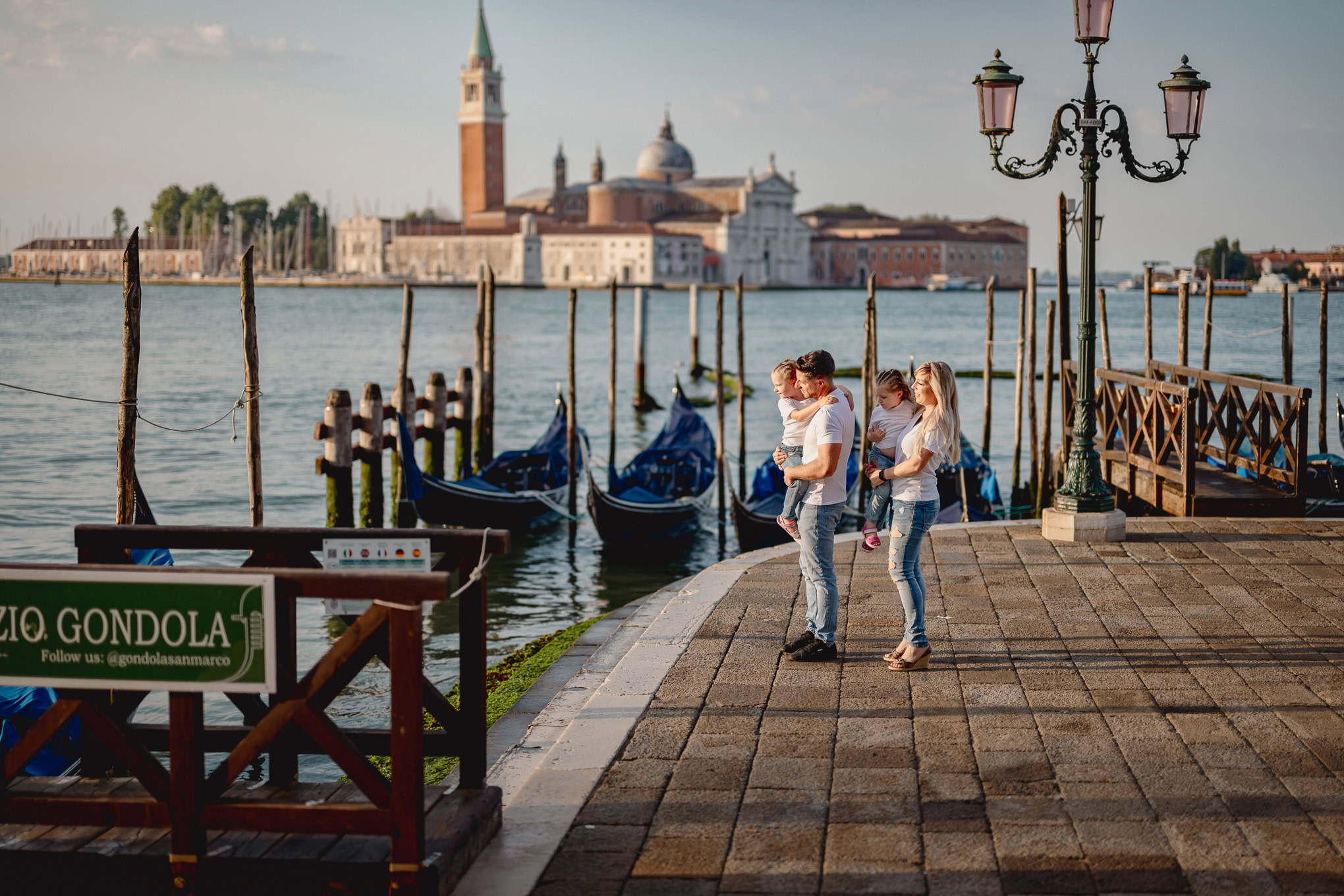 Family enjoying a walk along Venice's waterfront with gondolas and historic buildings in the background, bathed in soft.