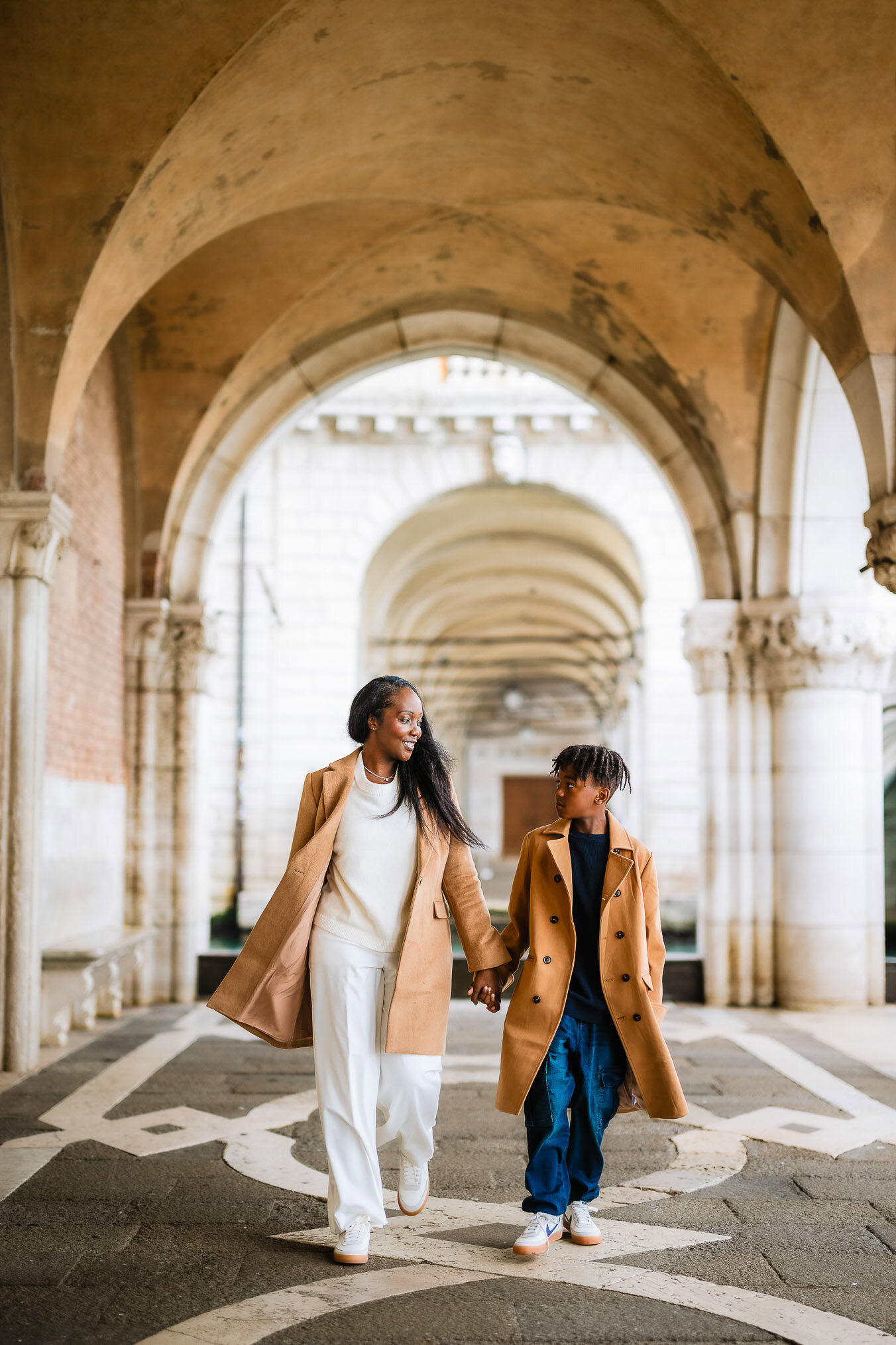 Family walking hand-in-hand through Venice's historic archways, enjoying the warm sunlight and charming surroundings.