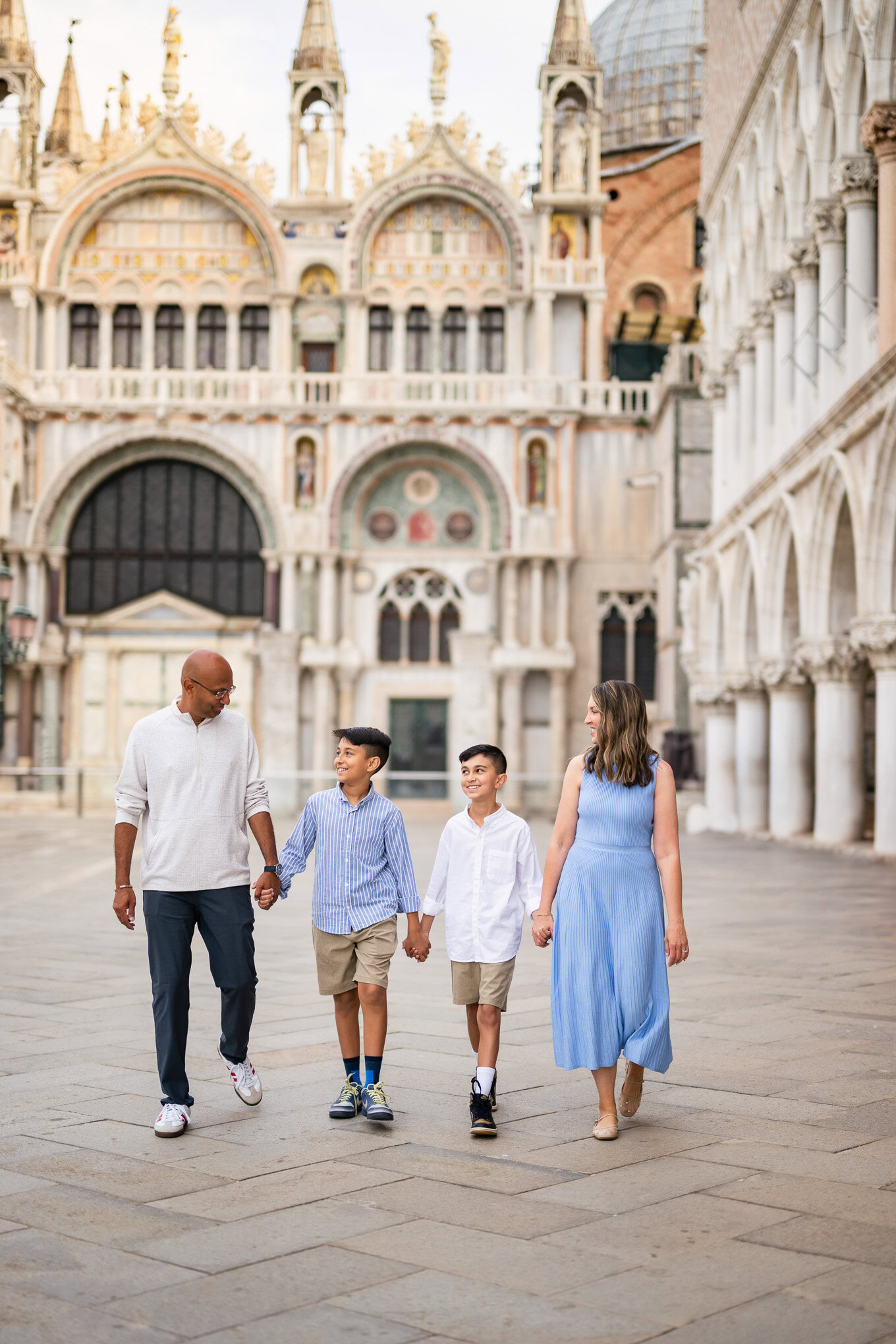 A family walking hand-in-hand through Venice's historic square, enjoying the warm sunlight and vibrant architecture arou.