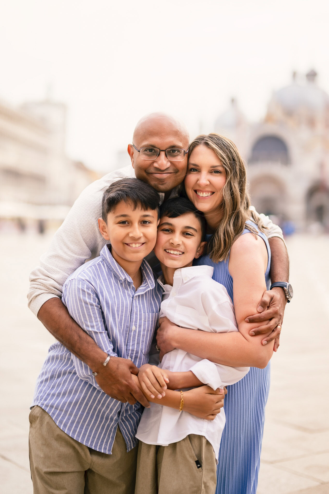 A family of four sharing a joyful moment together in Venice, with historic architecture and soft natural light in the ba.