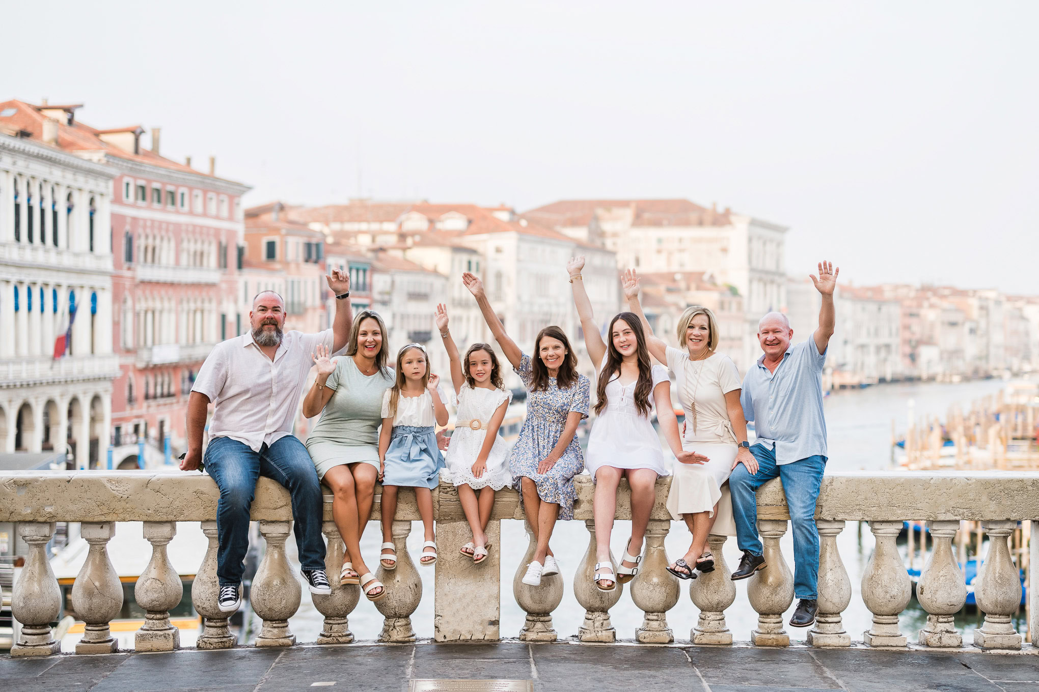 A family of nine enjoying a relaxed moment together on a Venetian canal bridge, with historic buildings and boats in the.