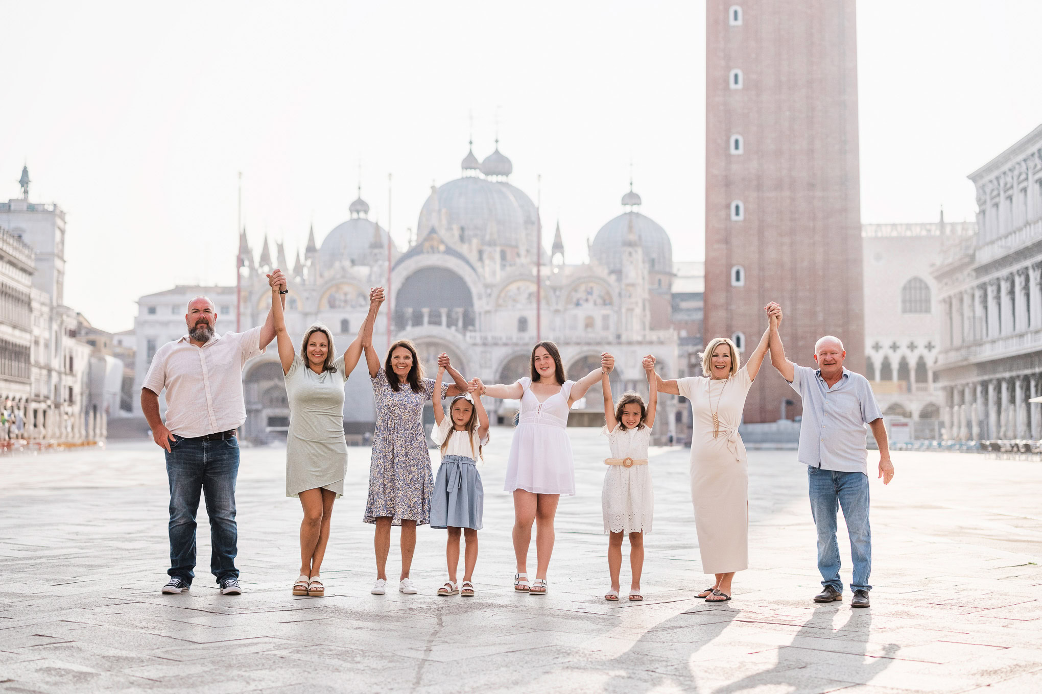 A family holding hands and smiling together in a spacious Venetian square with historic buildings and soft natural light.