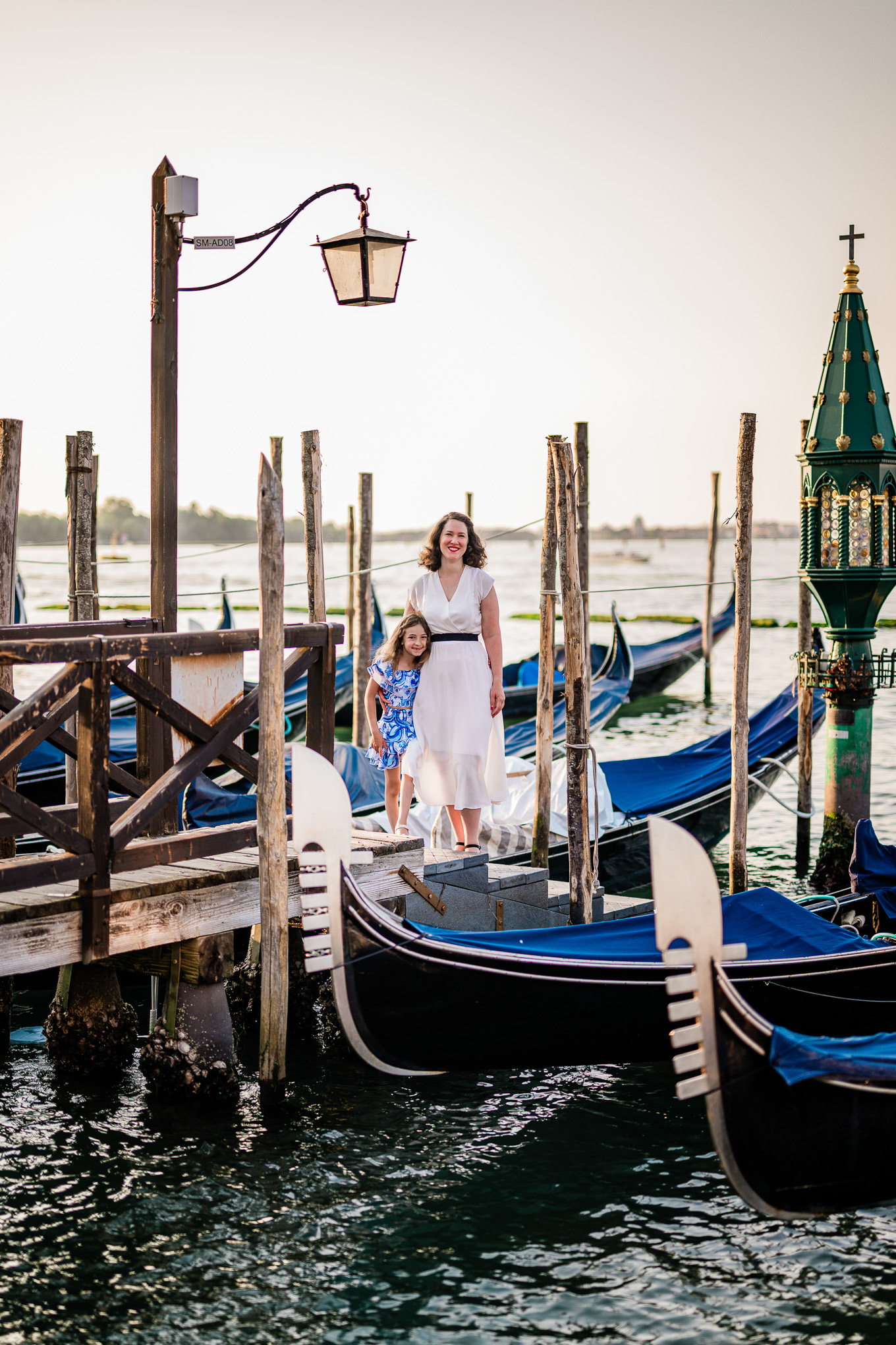 A family enjoying a peaceful moment on a Venice dock, with gondolas and historic lamp posts under soft natural light.