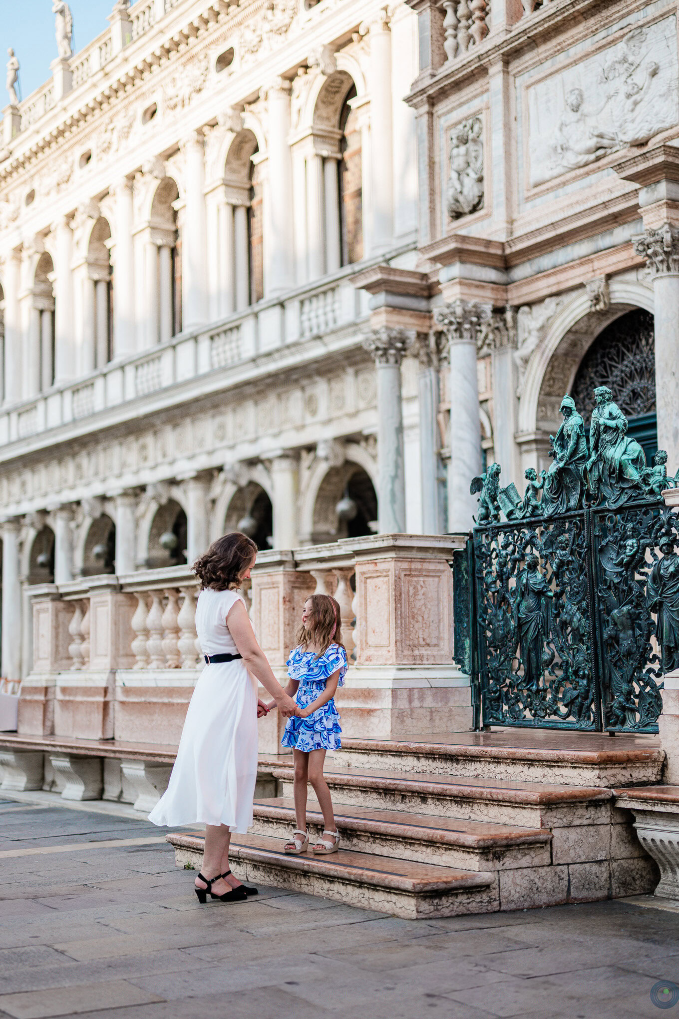 A woman and two children holding hands explore a historic Venetian building, bathed in warm sunlight, capturing a tender.