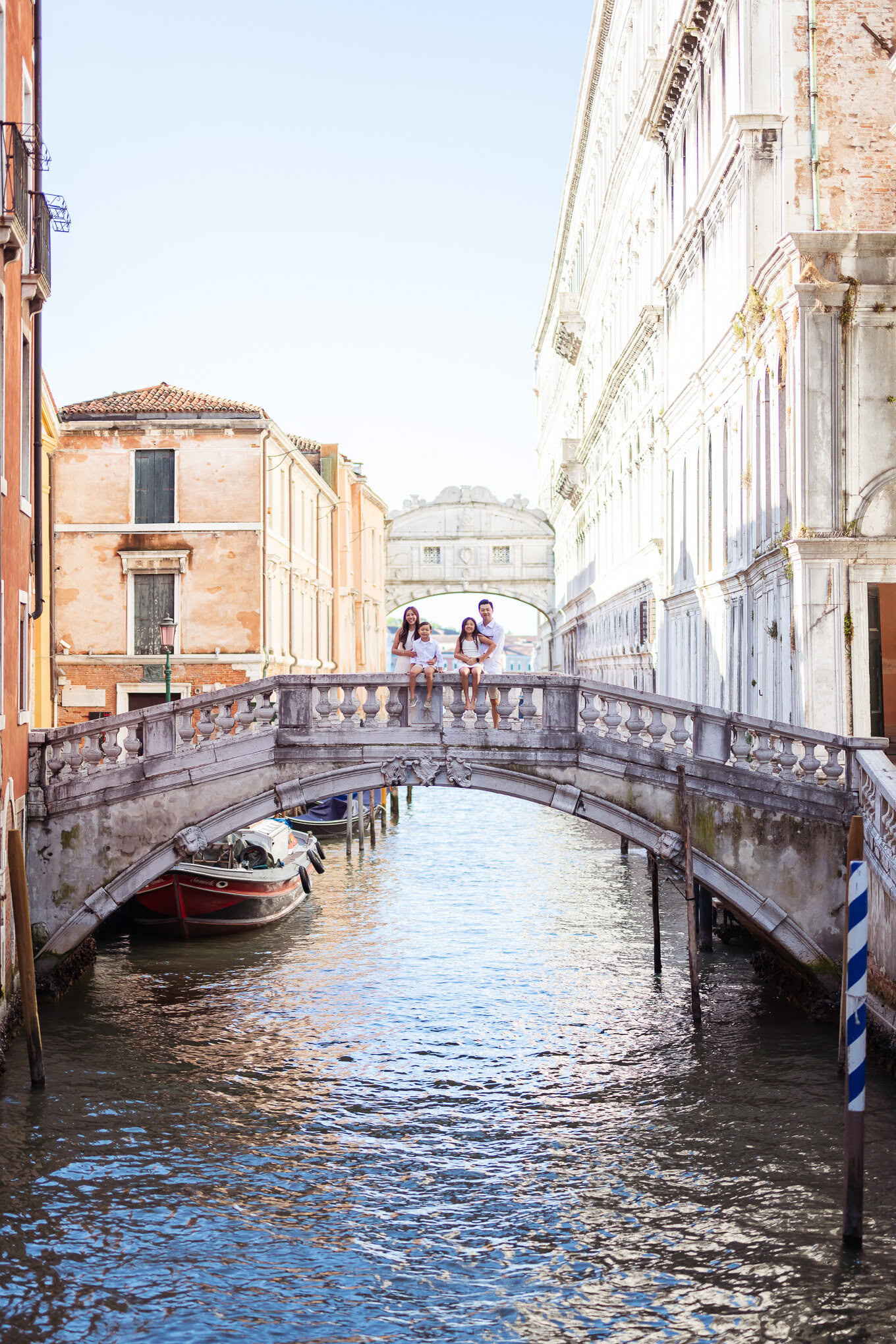 A family of four walking hand-in-hand across a small bridge over a canal in Venice, surrounded by historic buildings and.