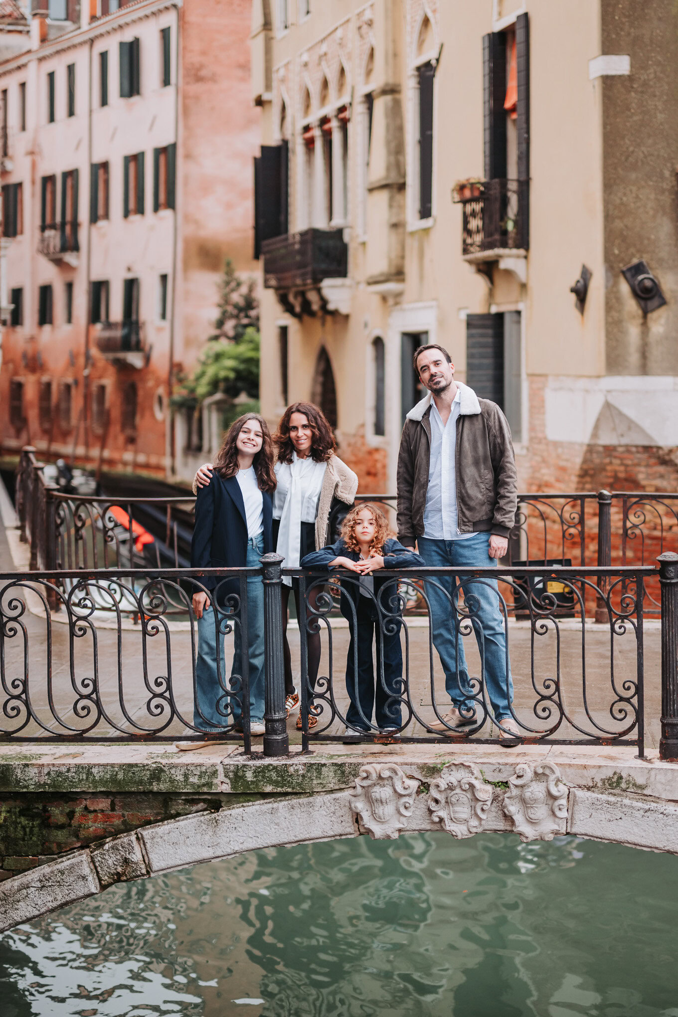A family of four enjoying a relaxed moment together on a bridge in Venice, surrounded by colorful historic buildings and.