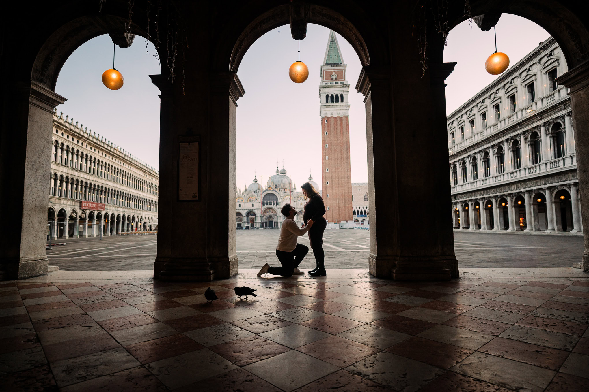 Family sharing a tender moment under Venetian arches with the bell tower in the background, illuminated by soft natural.