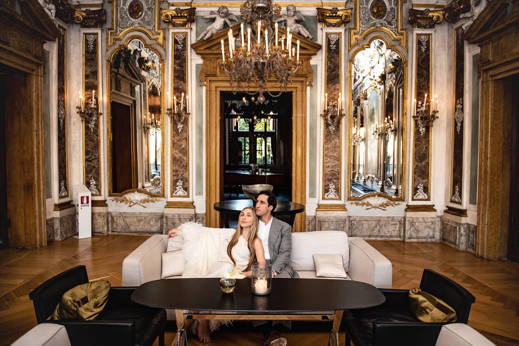 Couple sitting on a sofa in an elegant, historic Venetian interior with ornate details and warm ligh.