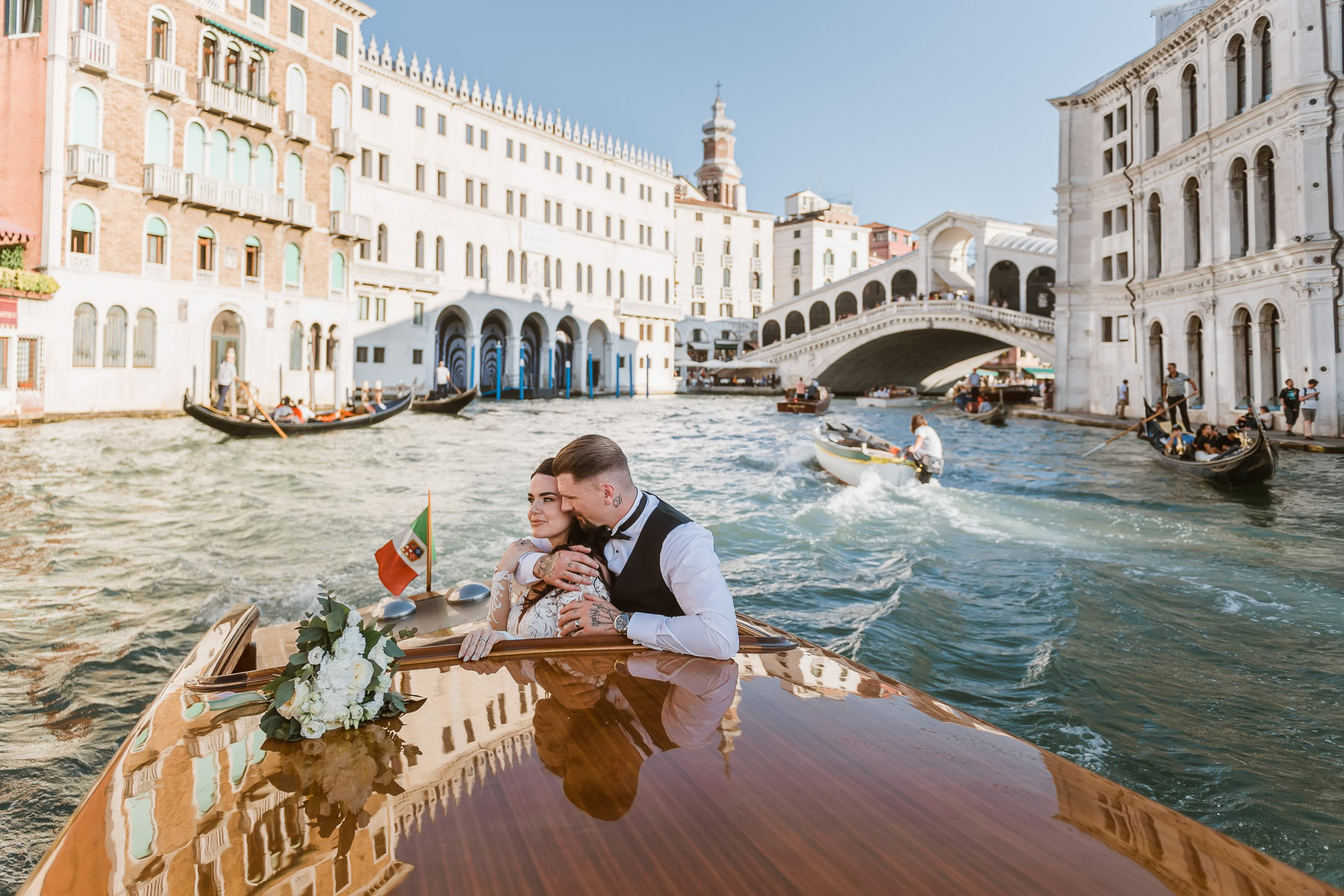 Couple enjoying a romantic moment on a taxi in Venice with historic architecture and calm waters.