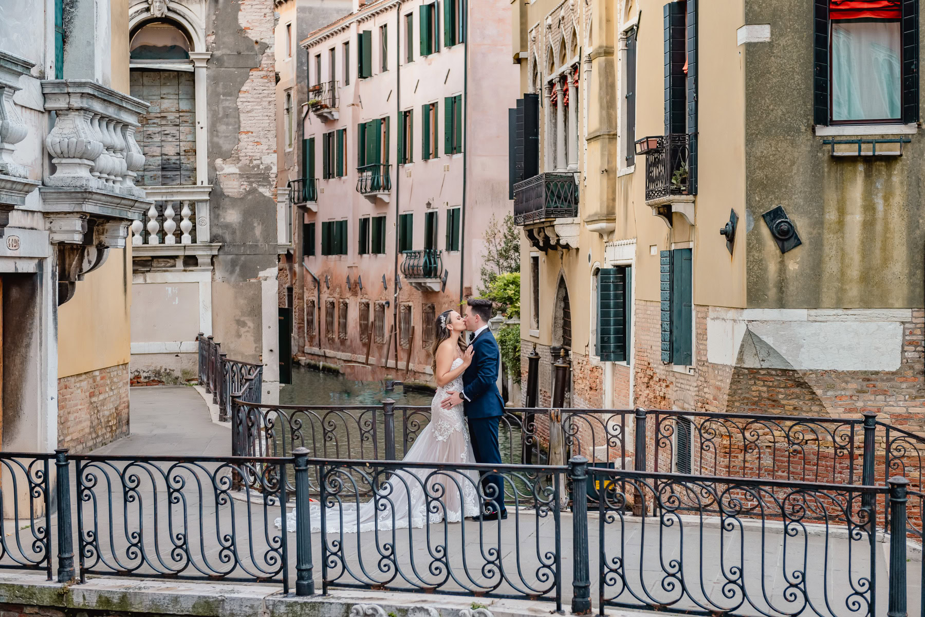 A couple in wedding attire sharing a moment on a Venice canal bridge at sunset.