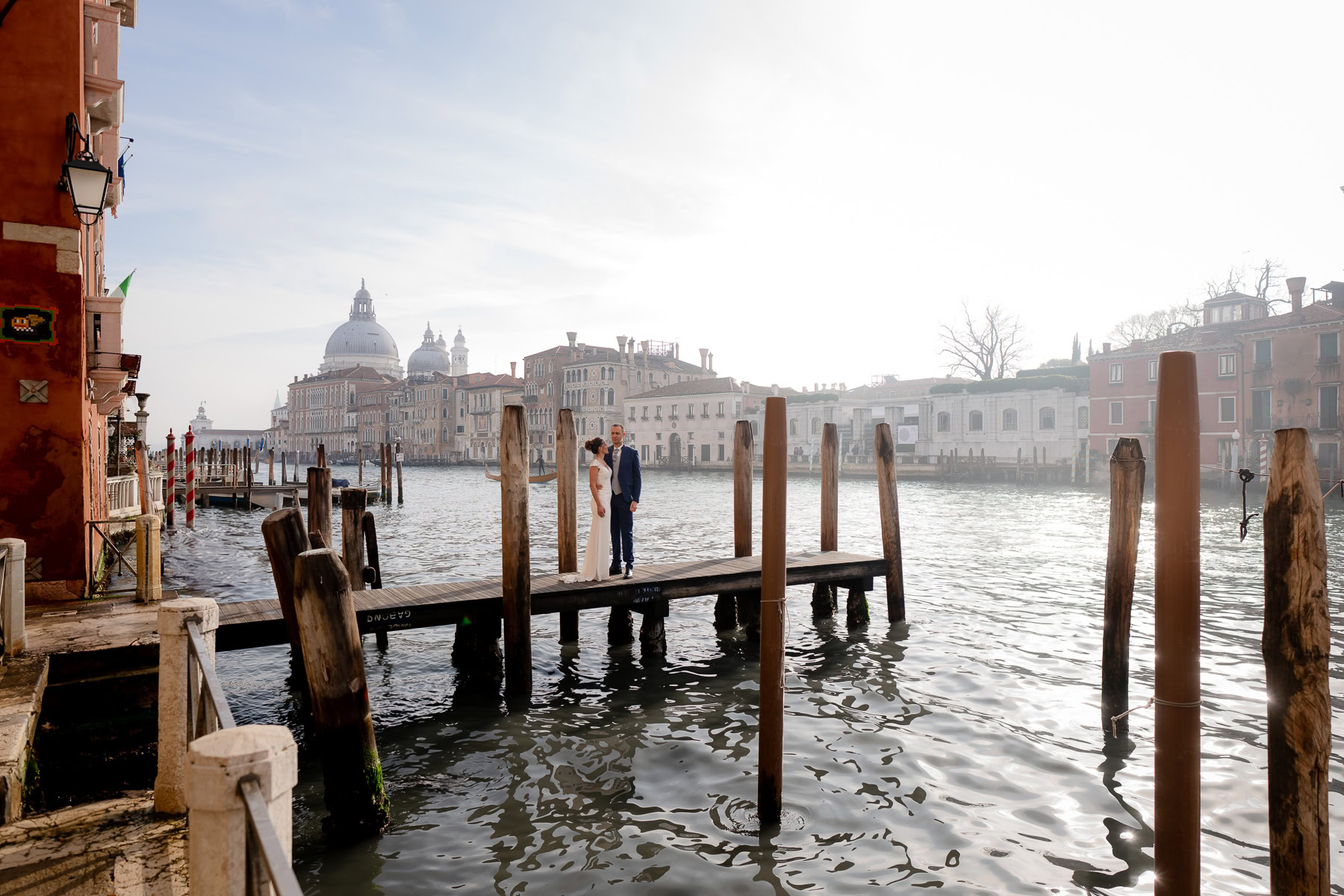 Two people on a Venice dock with historic cityscape and water in soft daylight.