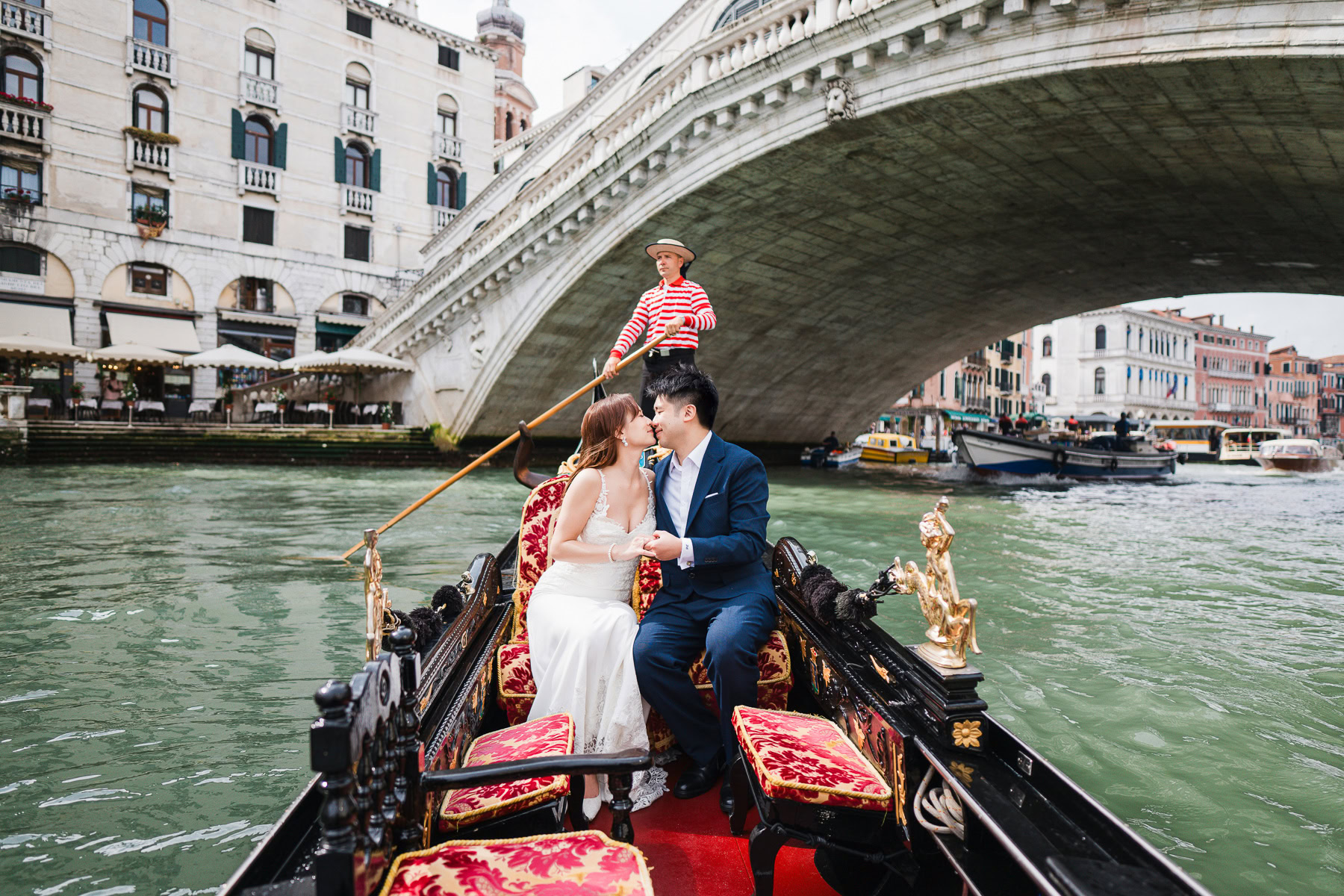 A couple enjoying a romantic gondola ride in Venice under a historic bridge at sunset.