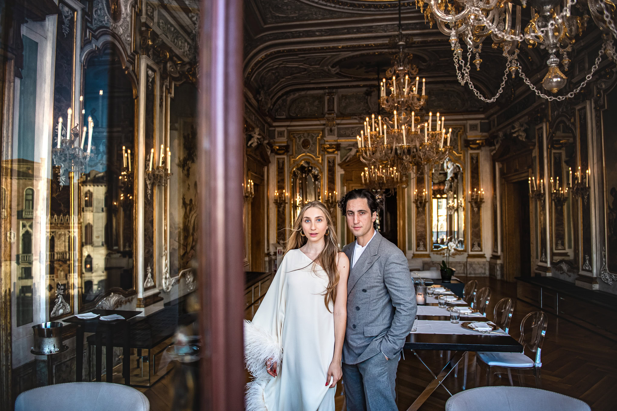 Romantic couple in elegant attire inside a luxurious Venetian palace with warm lighting and ornate decor.