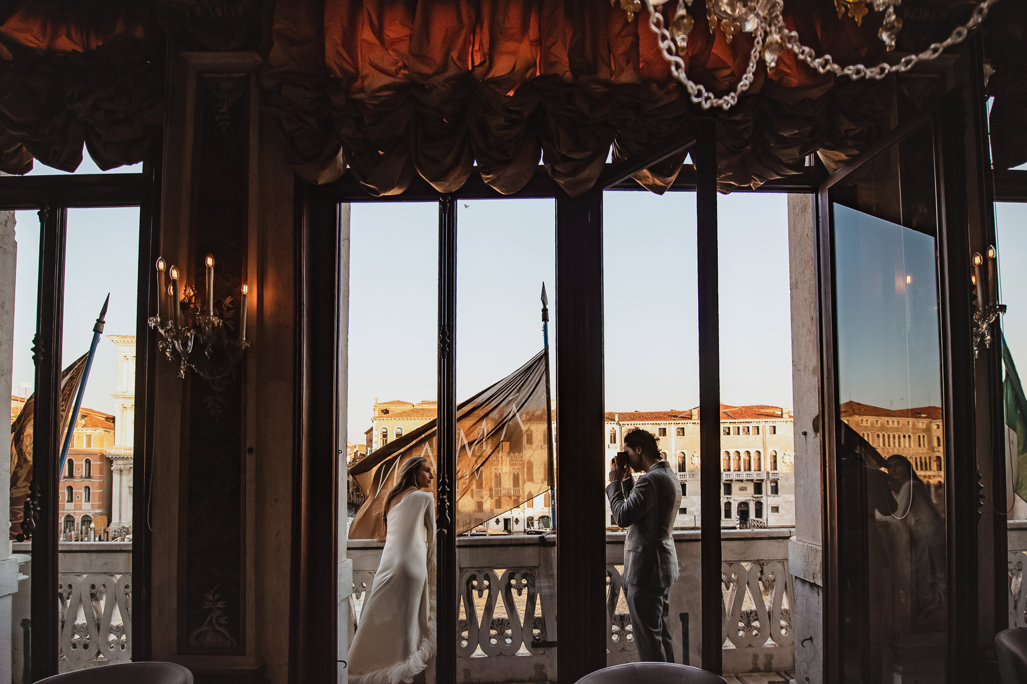A couple standing on a Venetian balcony, bathed in warm light, creating a romantic and intimate atmosphere.
