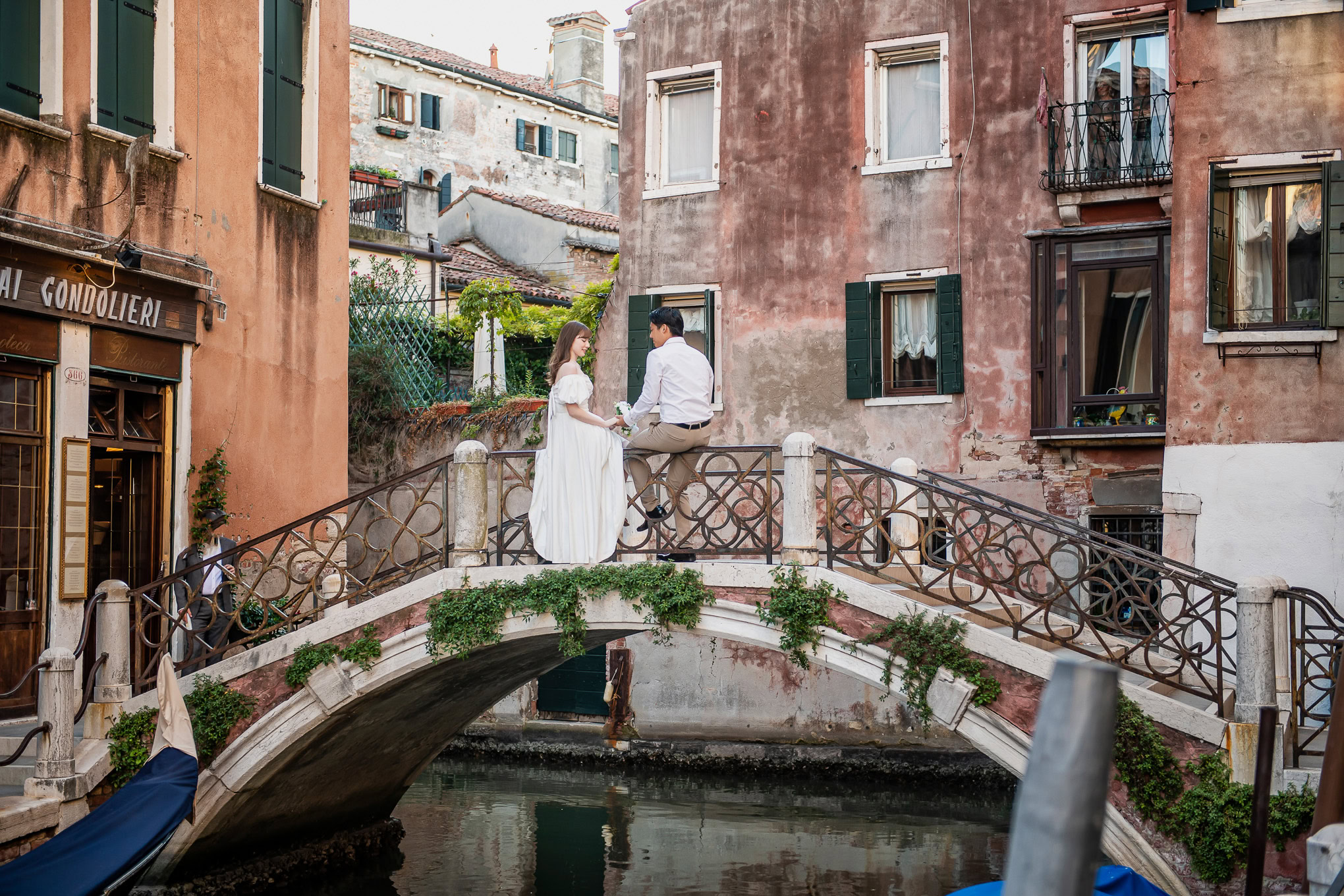 Romantic couple sitting on a bridge in Venice with warm light and colorful historic buildings in the background.