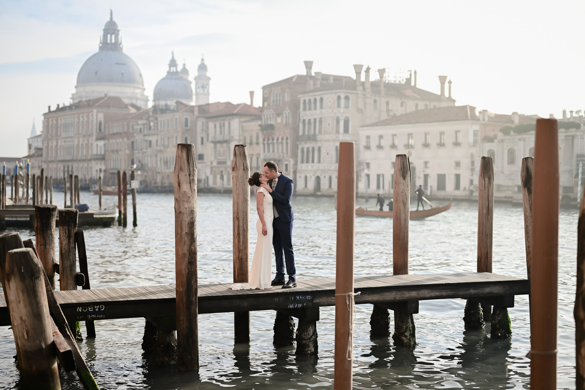 Romantic couple embracing on a Venice dock with historic cityscape and soft light in the background.