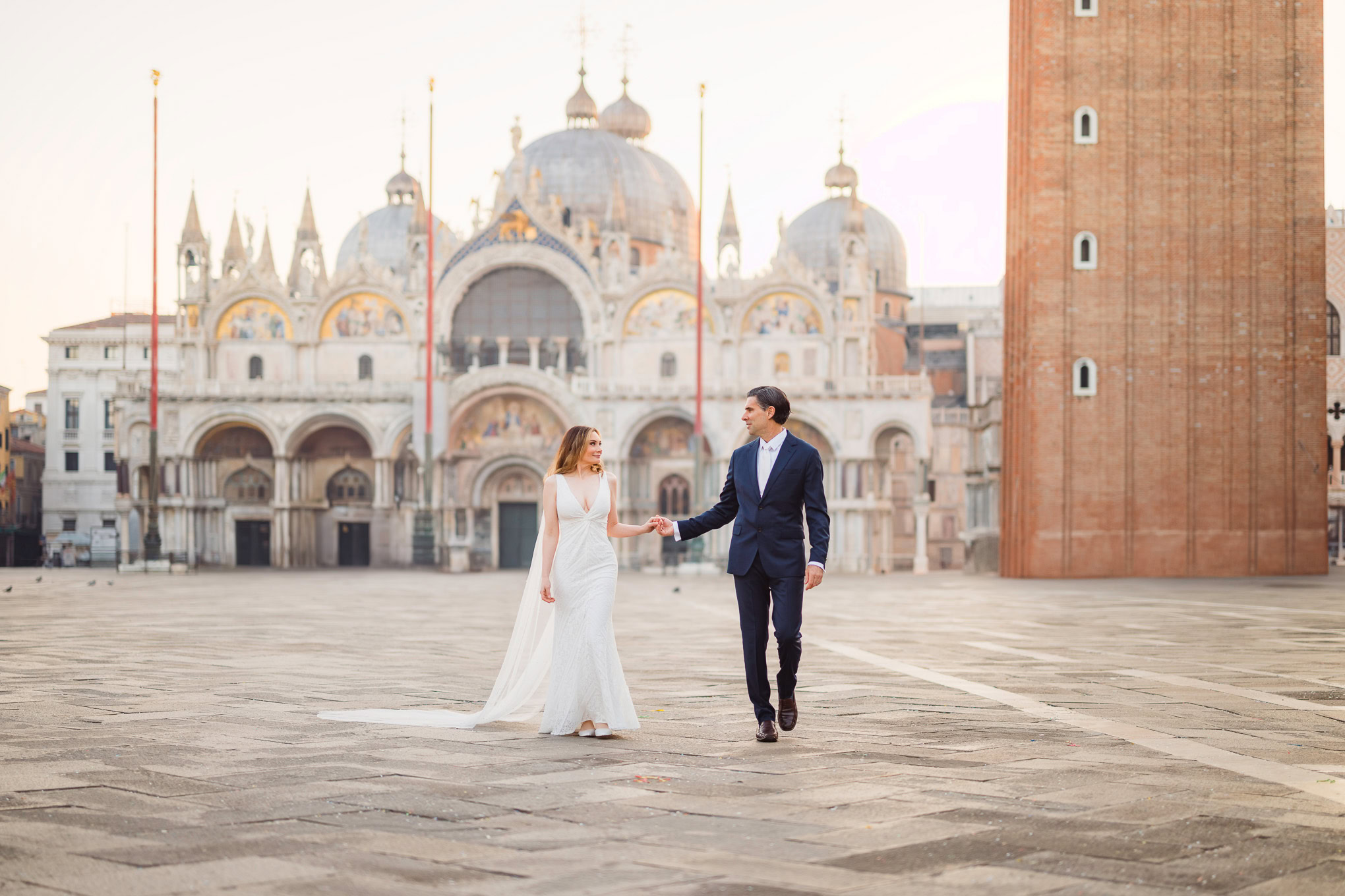 Romantic couple holding hands in Venice's historic square during golden hour, surrounded by warm, soft light and iconic.