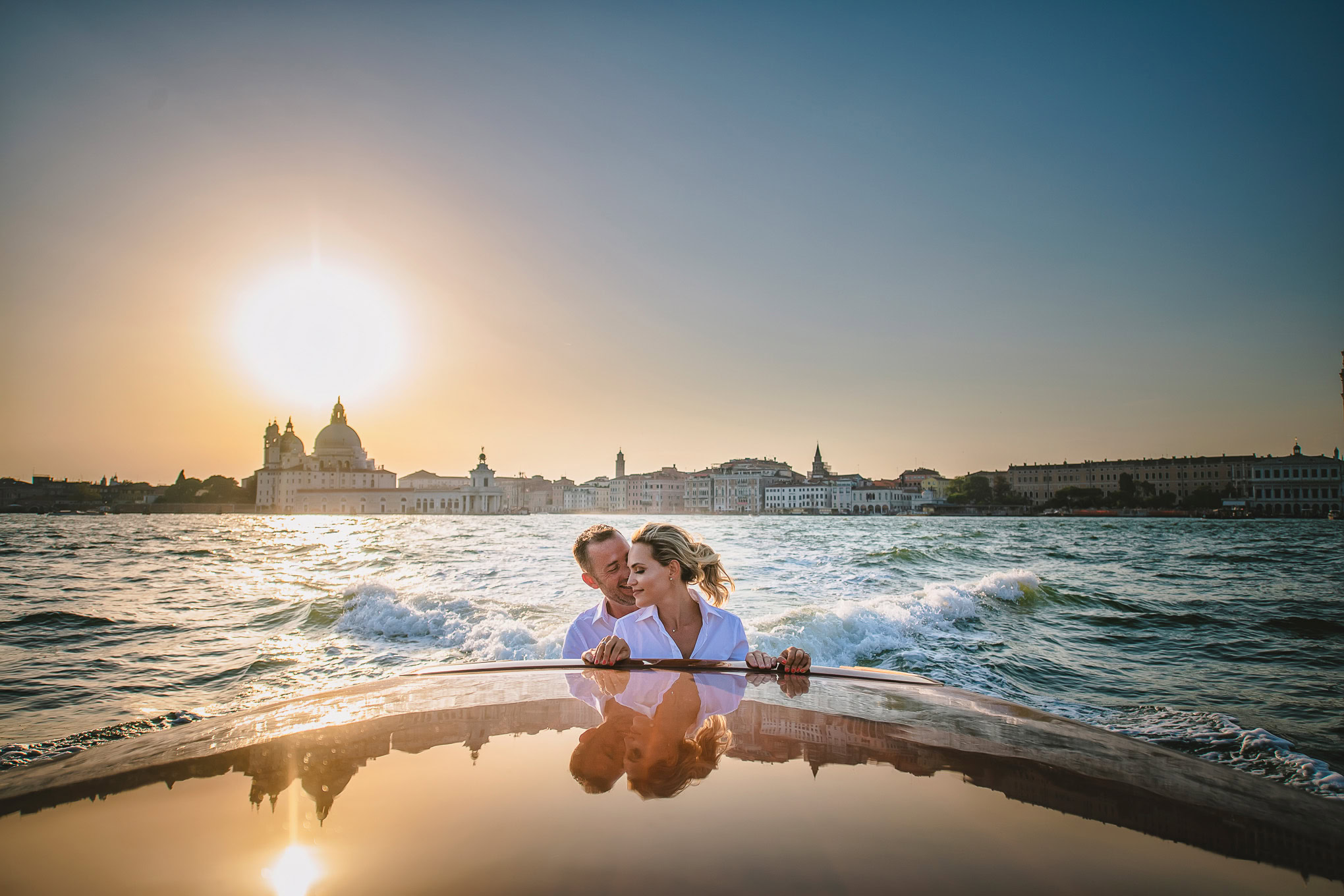 A couple enjoying a romantic moment on a boat in Venice at sunset, with warm light and serene water creating an intimate.