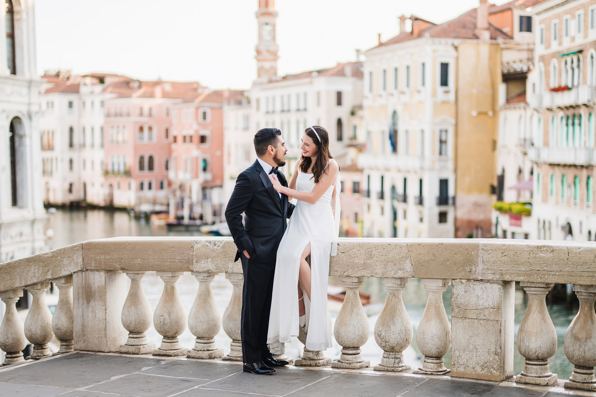 Romantic couple standing close on a bridge in Venice with soft natural light and colorful buildings in the background.