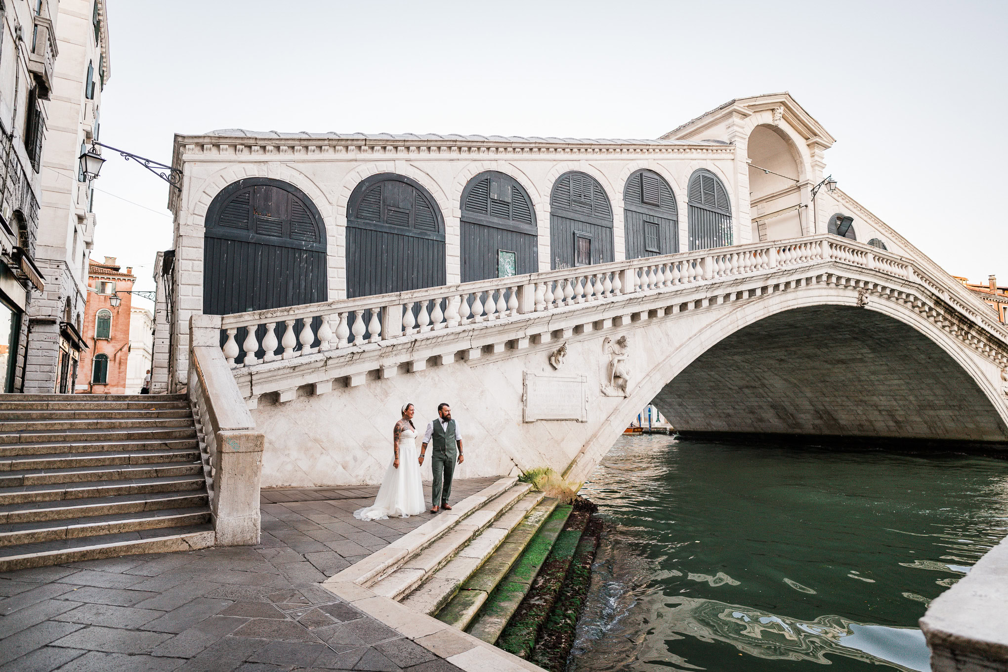 Romantic couple strolling along a Venice canal under soft sunlight, capturing a serene and intimate atmosphere.