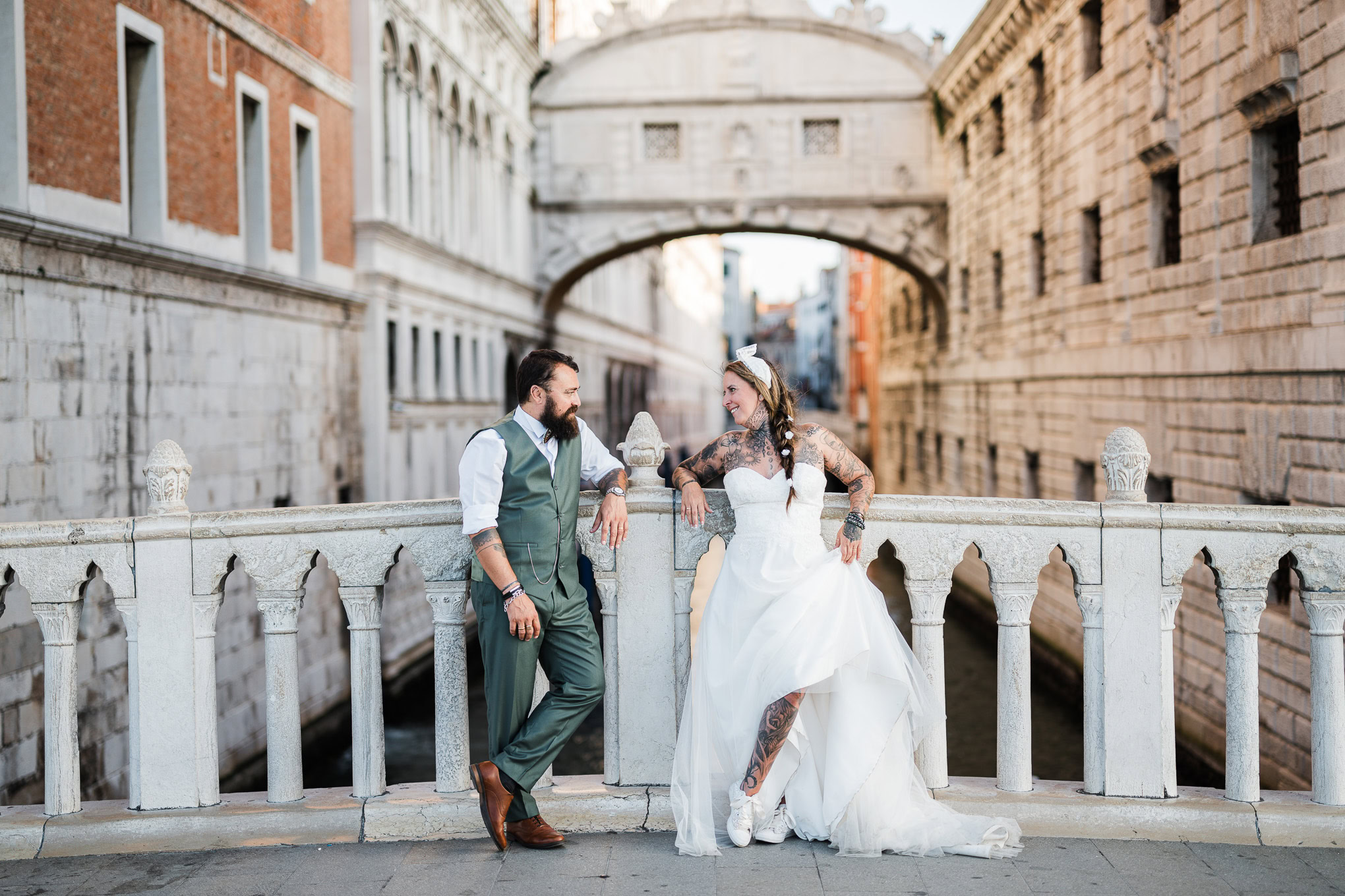 Romantic couple enjoying a peaceful moment on a Venice bridge with warm sunlight and historic architecture around them.