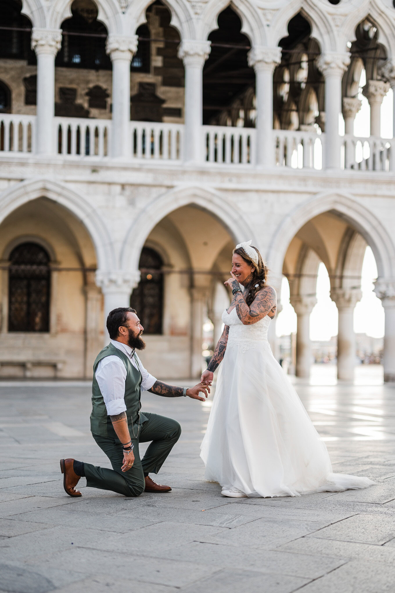Romantic couple in wedding attire sharing a tender moment beneath Venetian arches in soft, natural light.