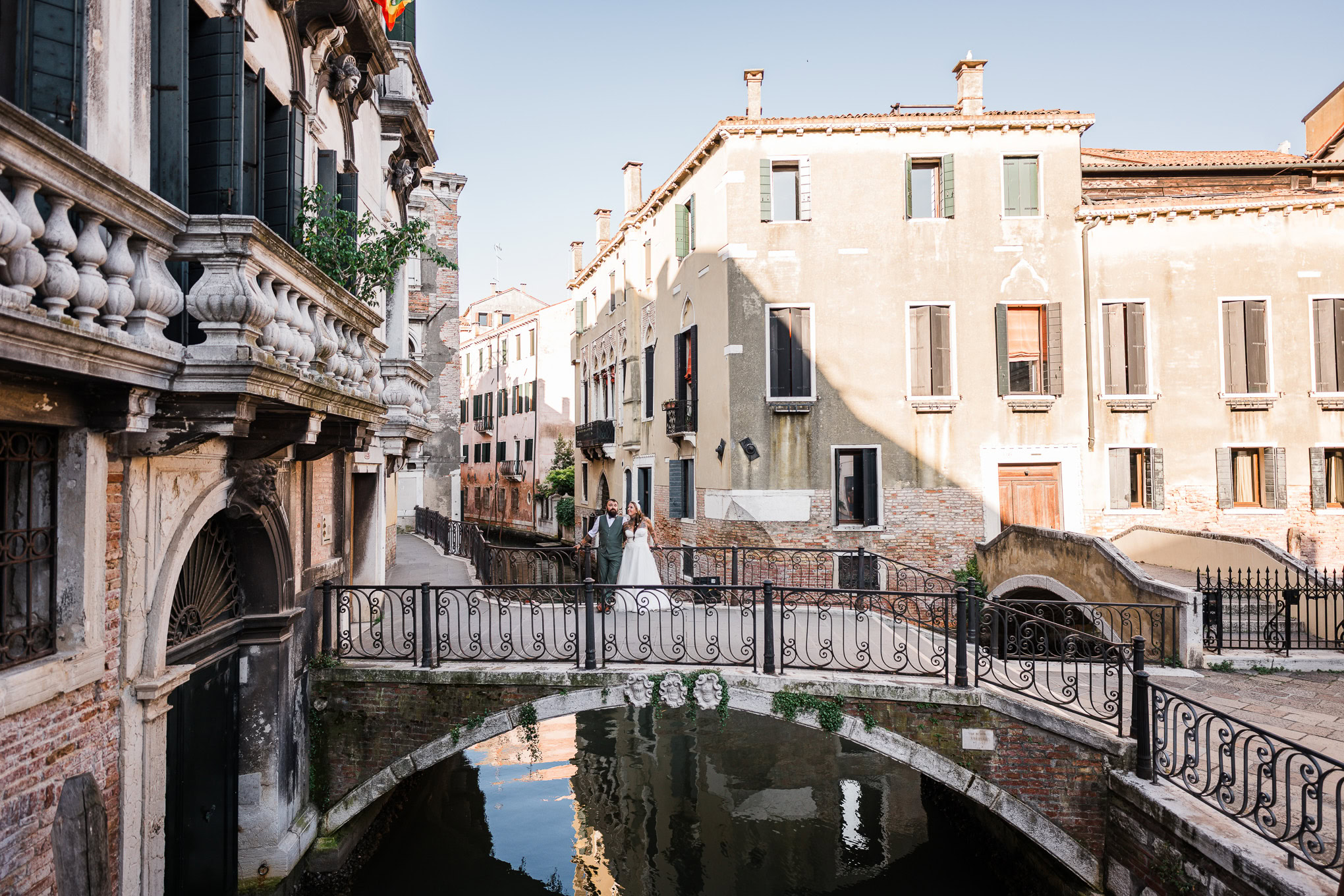 A couple walking hand in hand along a quiet canal in Venice, bathed in warm, golden light, creating a romantic and seren.