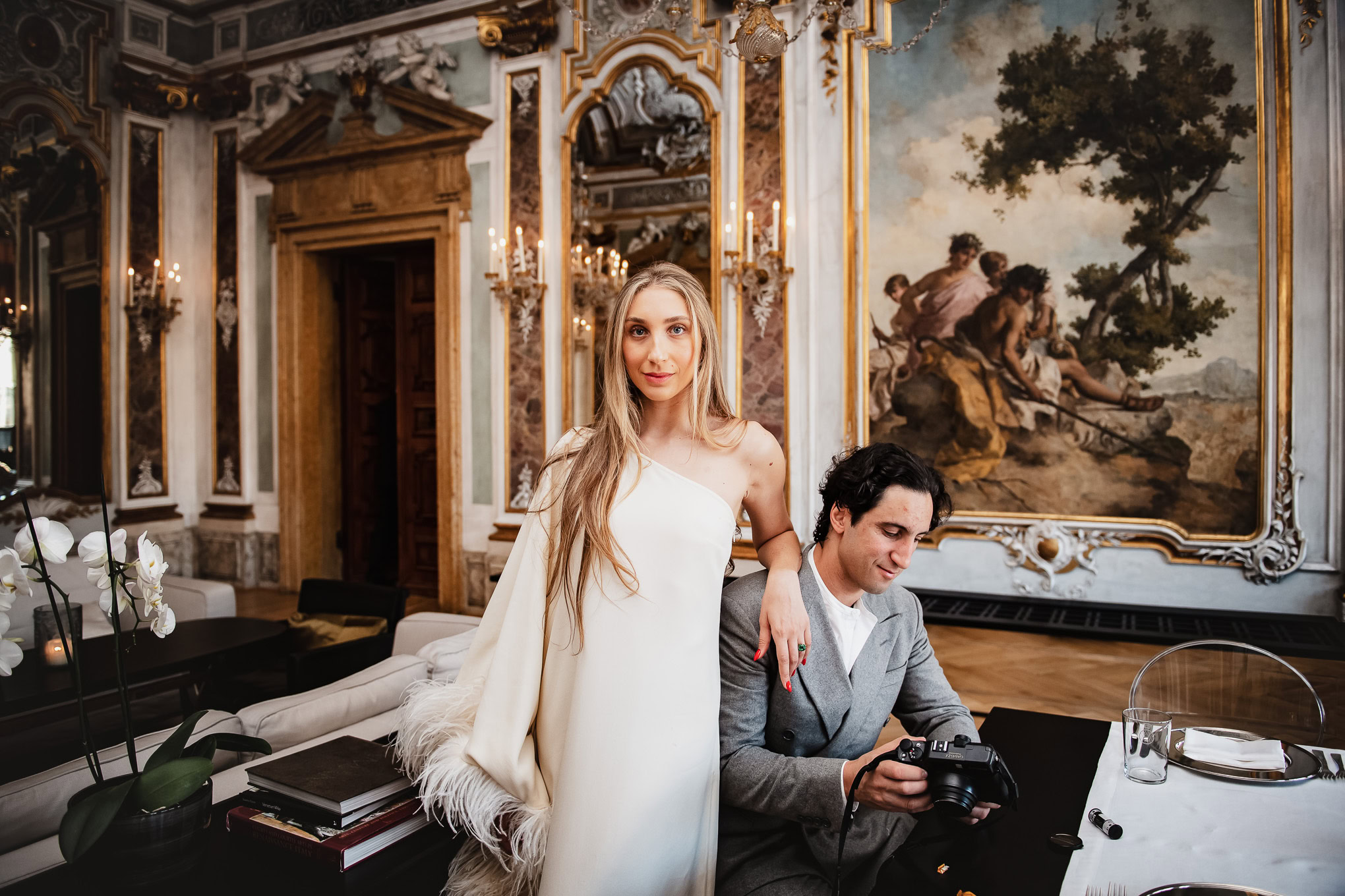 A romantic couple in elegant attire enjoying a serene moment in a luxurious Venetian interior with classical artwork.
